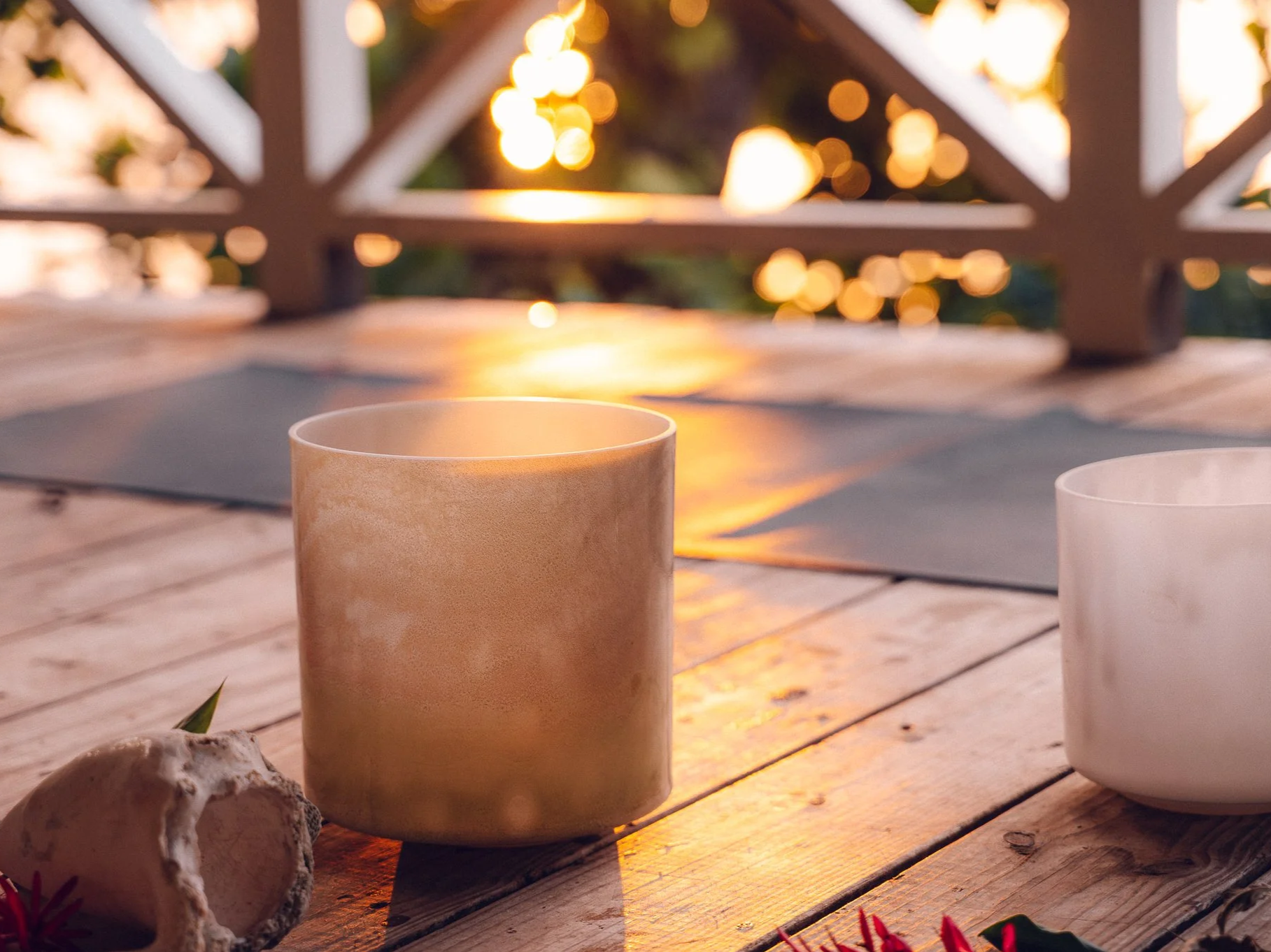 Two ceramic cups on a wooden table at sunset, with blurred background of a deck railing and warm bokeh lights.