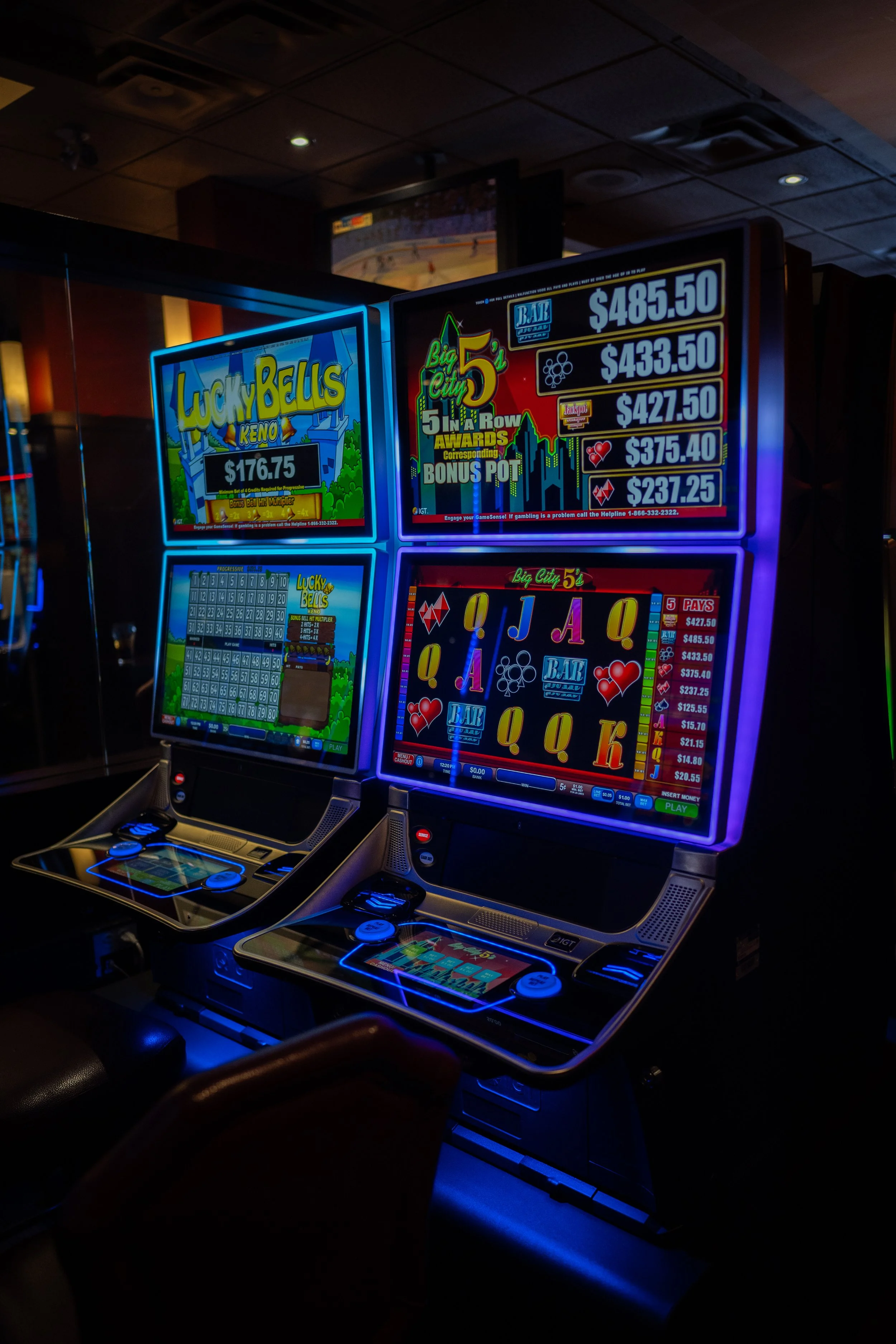 Two brightly lit slot machines inside a casino, with colorful screens displaying different games and payout amounts.
