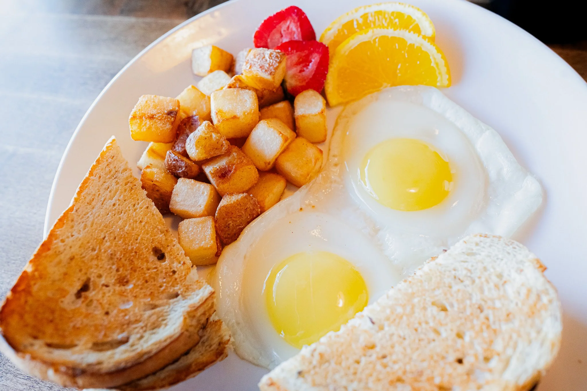 Breakfast plate with two sunny side up eggs, toasted bread, hash browns, and slices of orange and strawberries.