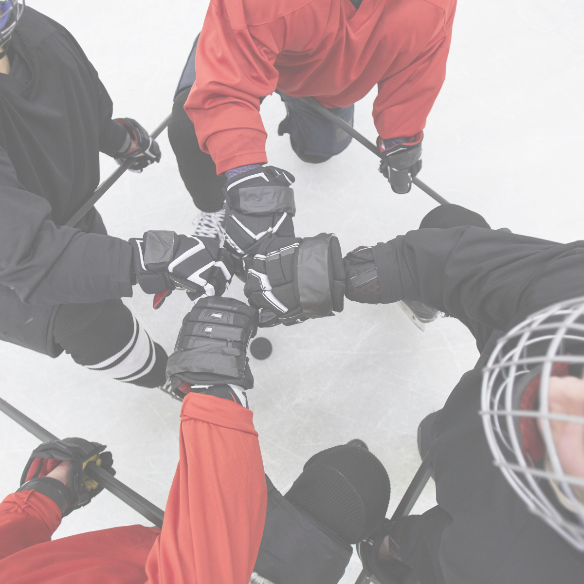 A group of hockey players in gloves and gear on an ice rink, forming a huddle and holding their sticks together in the center.