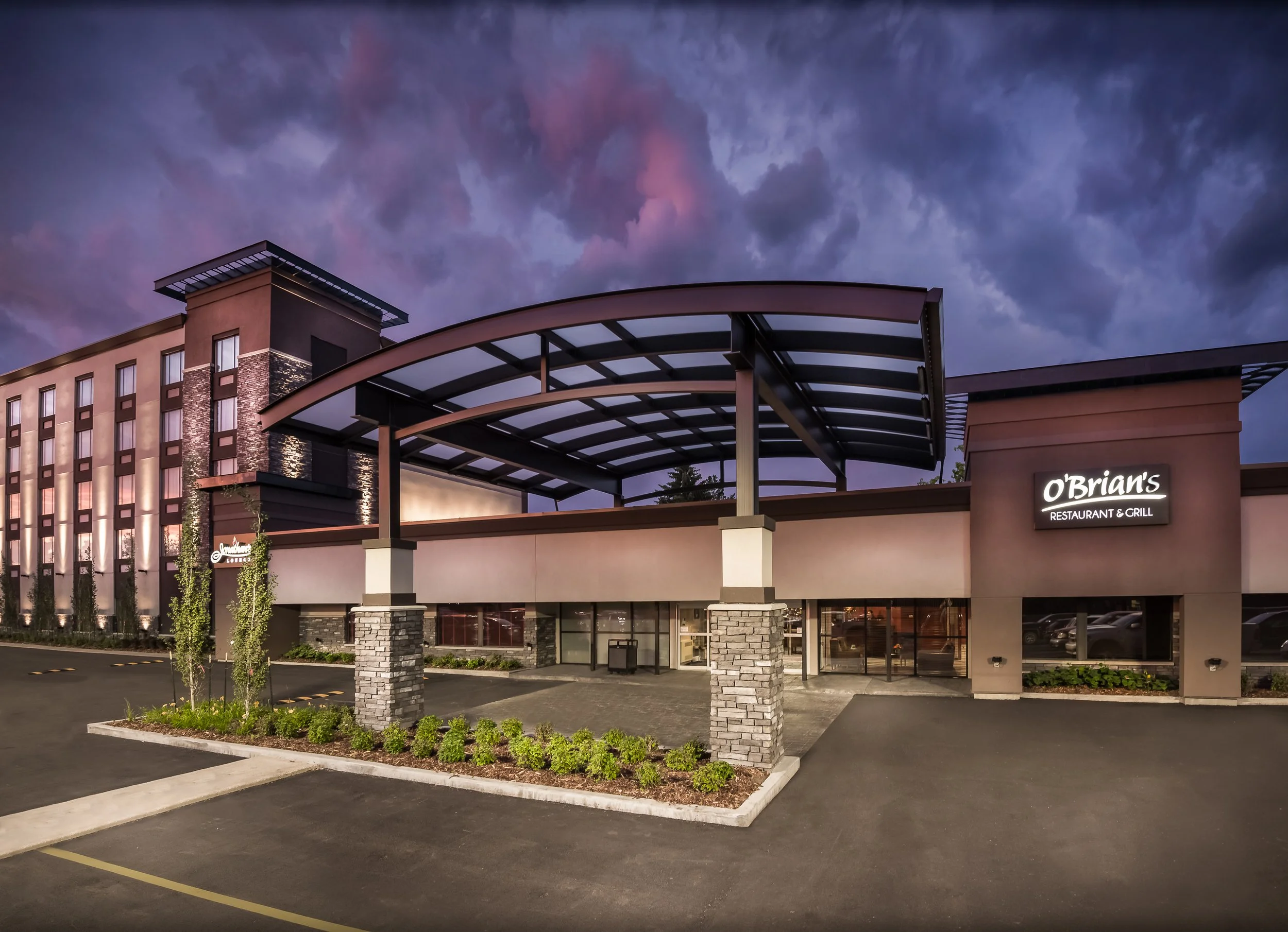 Exterior view of O'Brien's Restaurant & Grill during dusk, with a parking lot and landscaped area in the foreground, and a cloudy sky overhead.