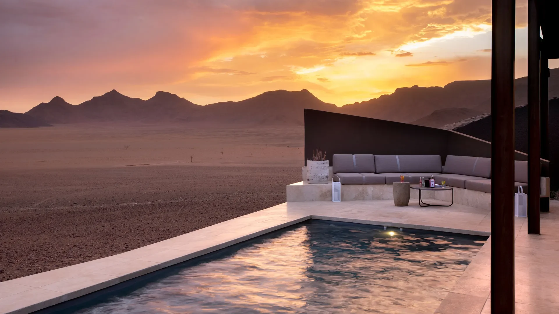 Luxury outdoor seating area with a pool in a desert landscape at sunset.