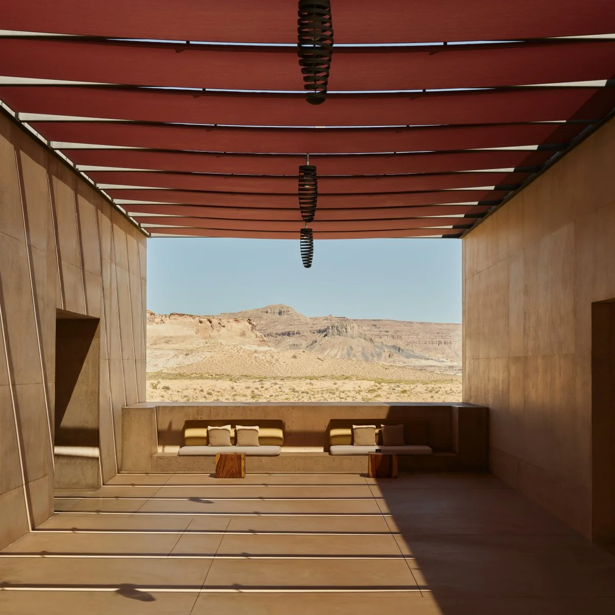 View from a modern structure with an open wall overlooking a desert landscape with mesas and a clear blue sky.