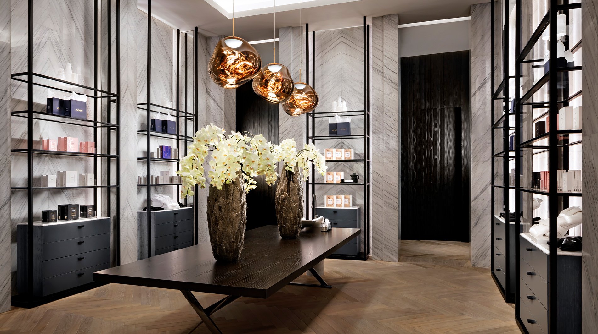 Interior of a modern retail store with display shelves, decorative vases with flowers on a wooden table, and pendant lights.