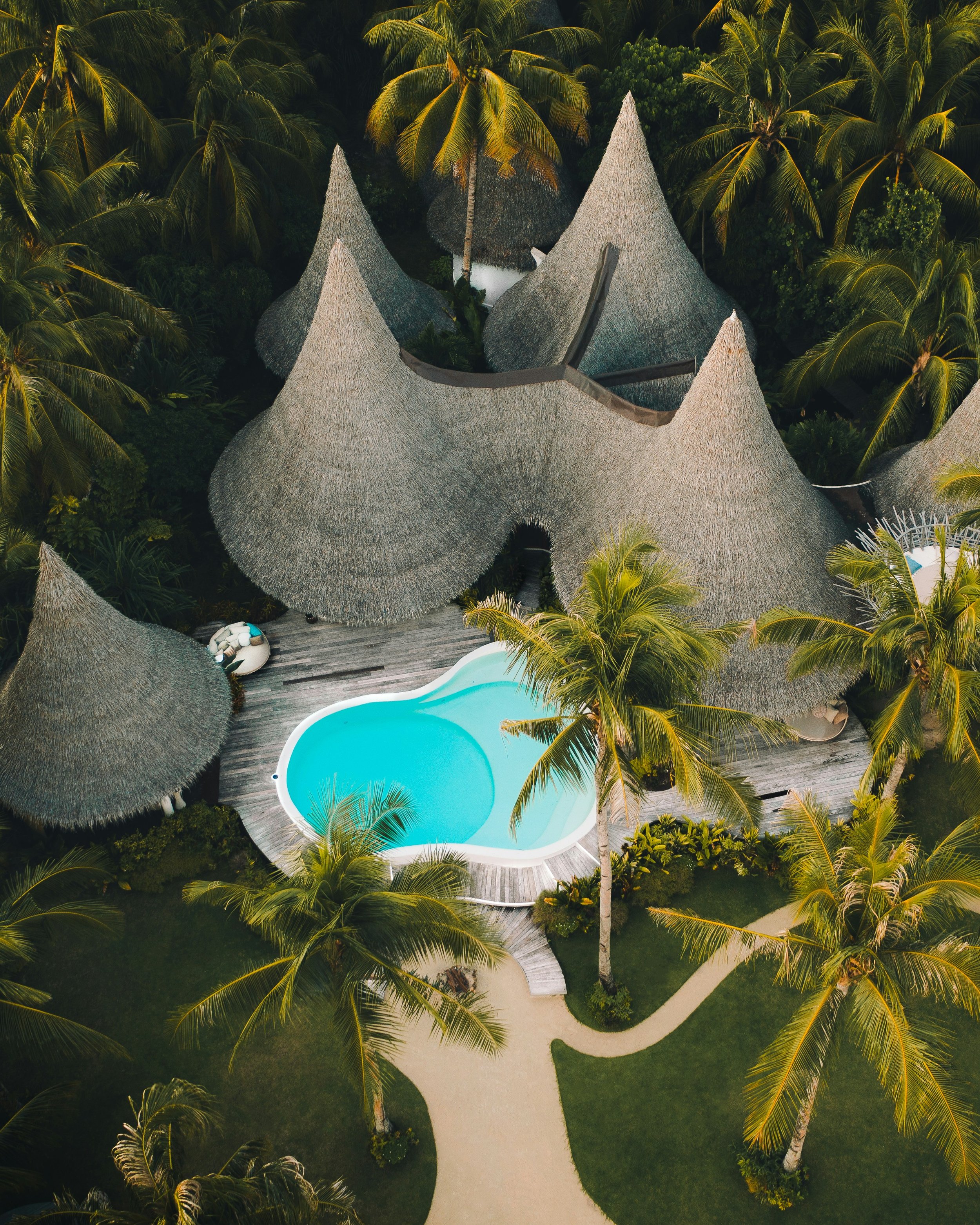 Aerial view of a tropical resort with a heart-shaped swimming pool, surrounded by palm trees and thatched-roof buildings.