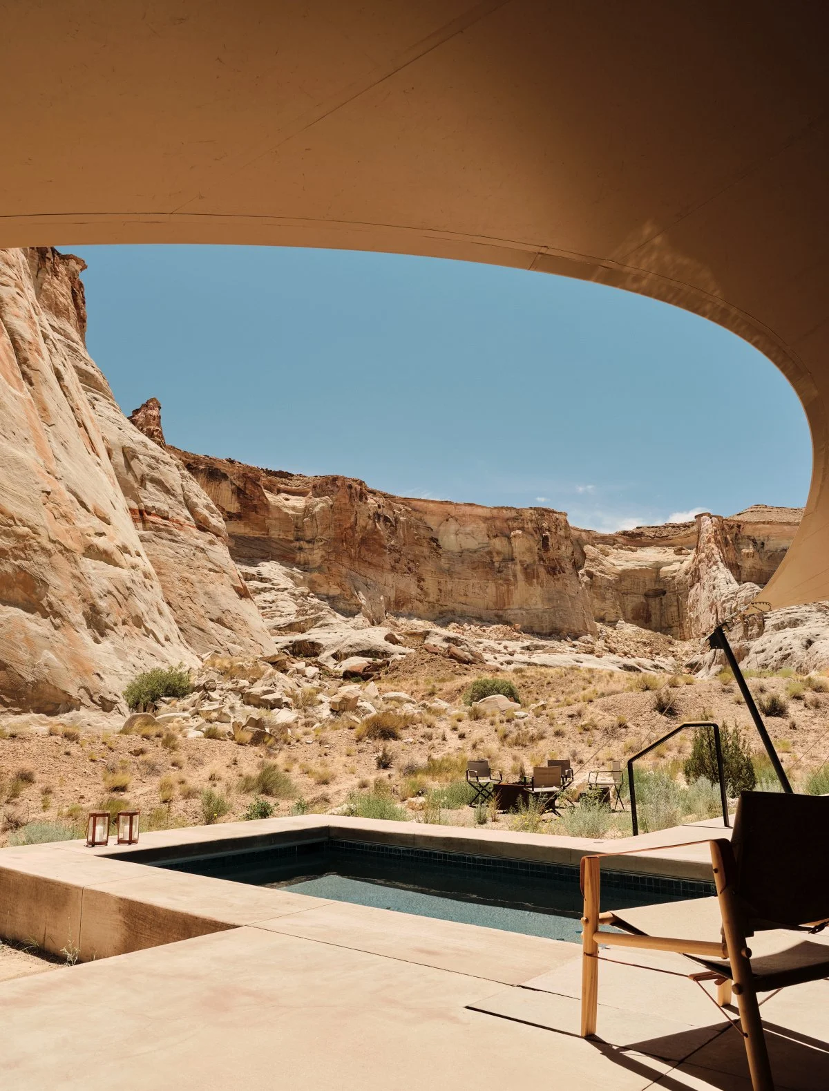 View of a desert canyon with rugged cliffs under a clear blue sky, seen from a shaded patio with a small pool and outdoor chairs.