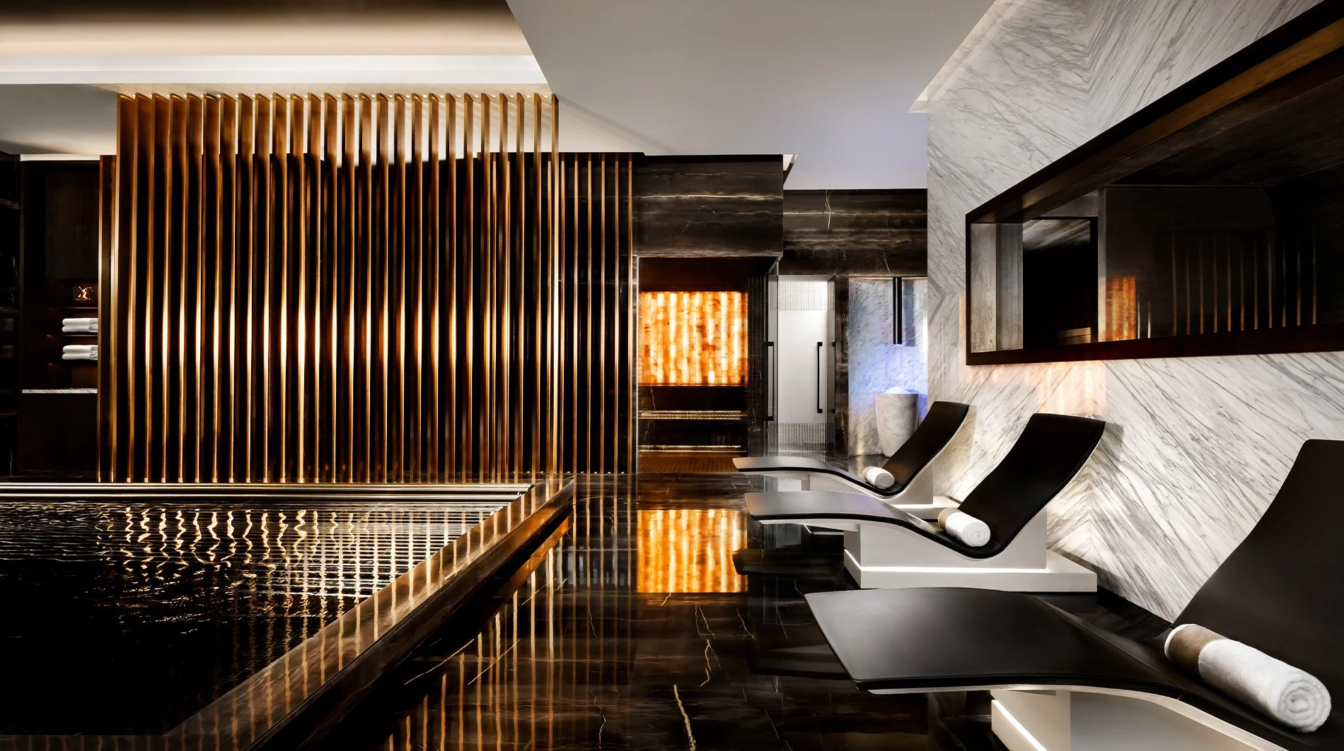 Indoor spa with black lounge chairs, marble walls, and wooden decorative slats.