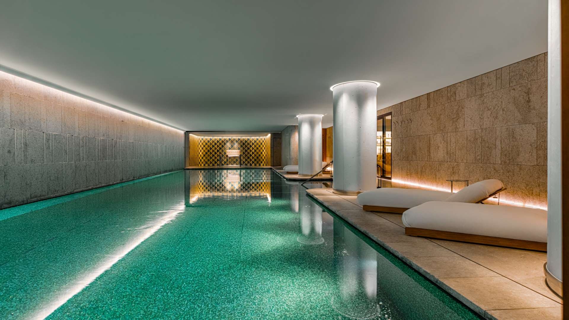 Luxurious indoor swimming pool with calm water, modern lounge chairs, and soft ambient lighting.
