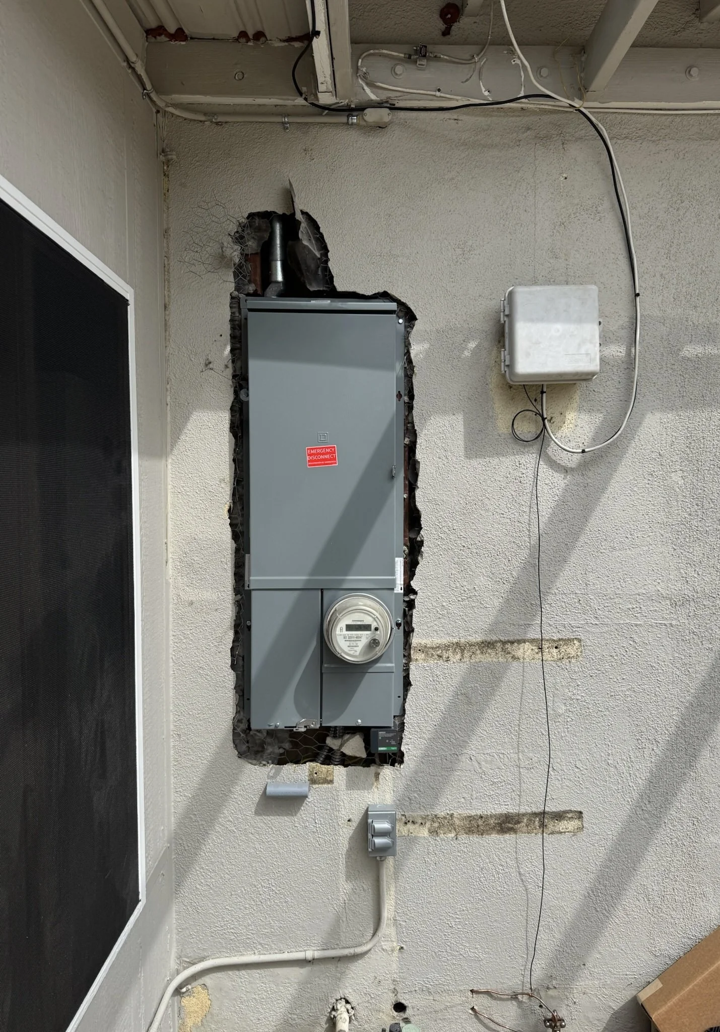 Electrical meter and panel mounted on a wall with a hole in the wall around the panel.