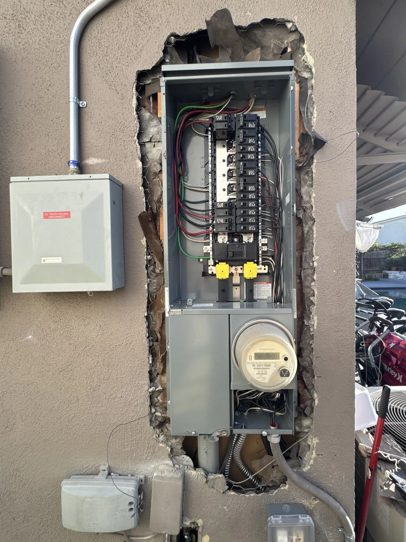 Electrical meter, circuit breakers, and wiring inside an open electrical panel on a wall.