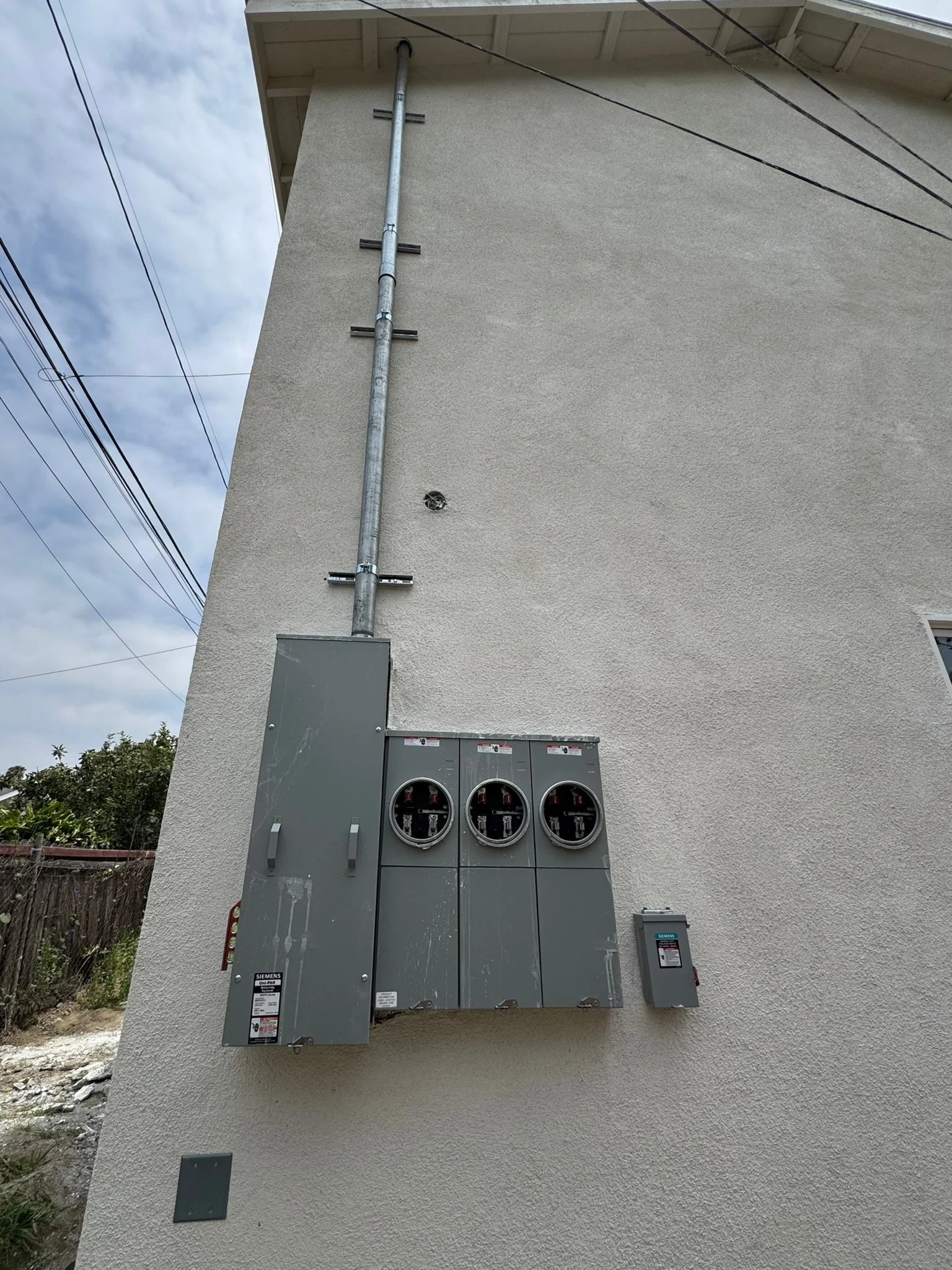 Electrical meter box and conduit on the exterior wall of a building with power lines overhead.