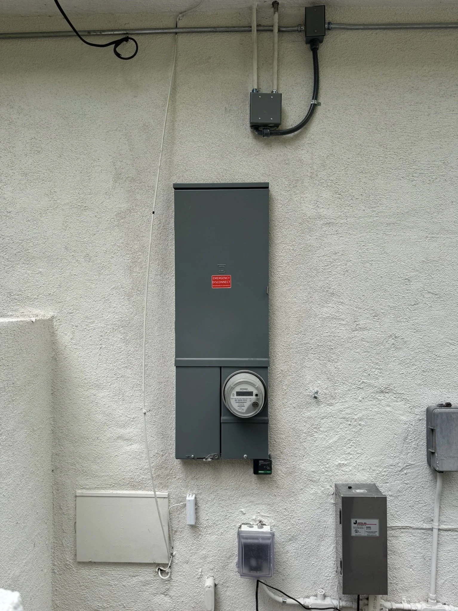 Electrical meter and gray electrical boxes mounted on a textured white wall.