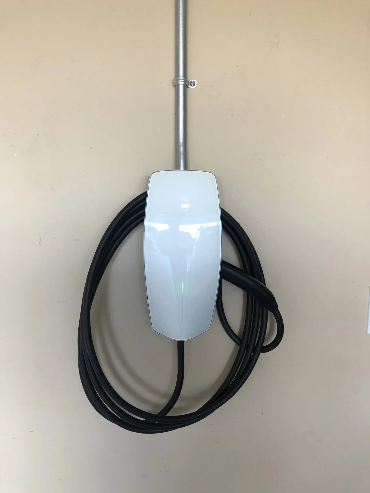 Electric vehicle charging station mounted on a beige wall with an attached cable.