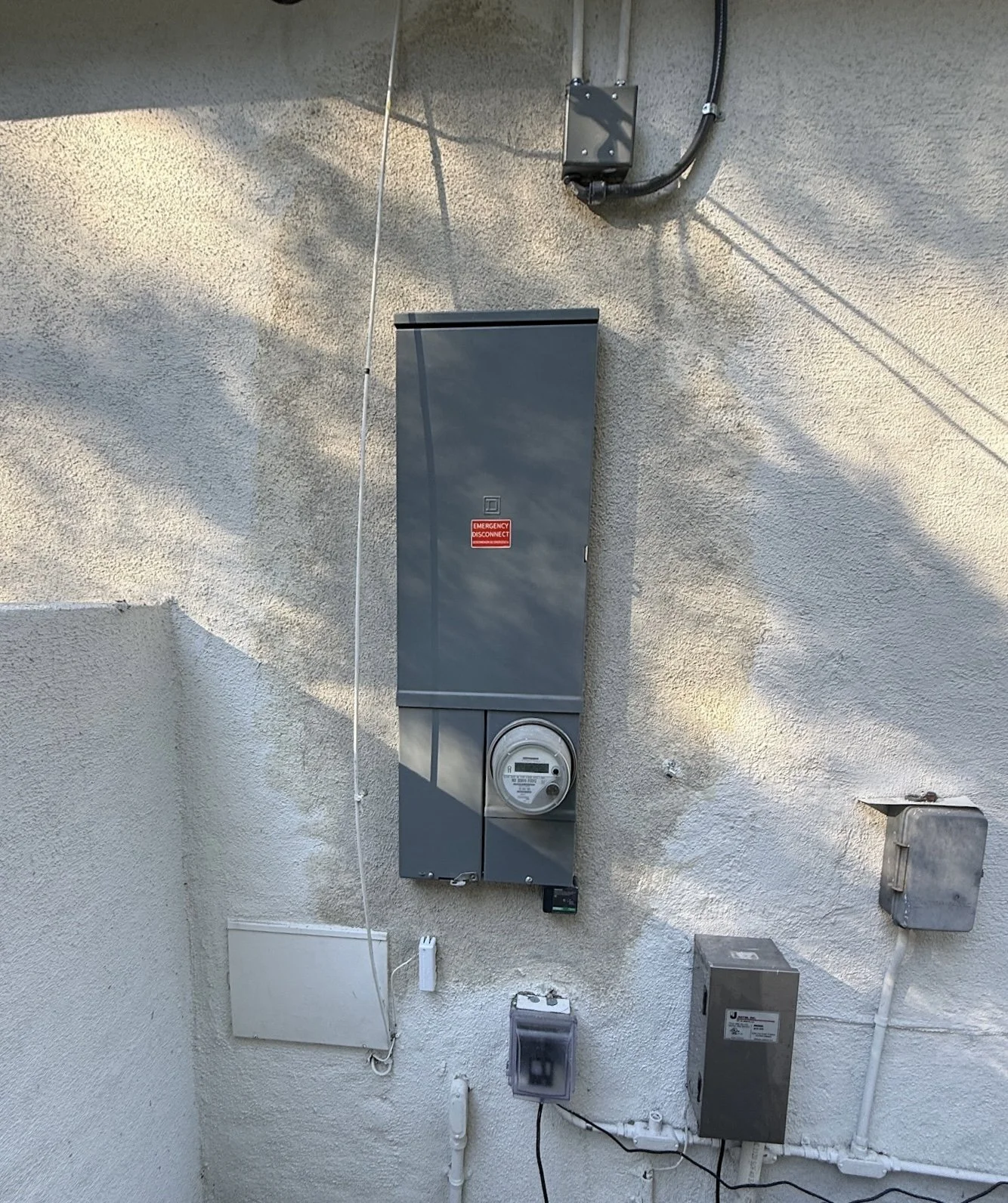 Electrical meters, boxes, and conduits mounted on a textured exterior wall.