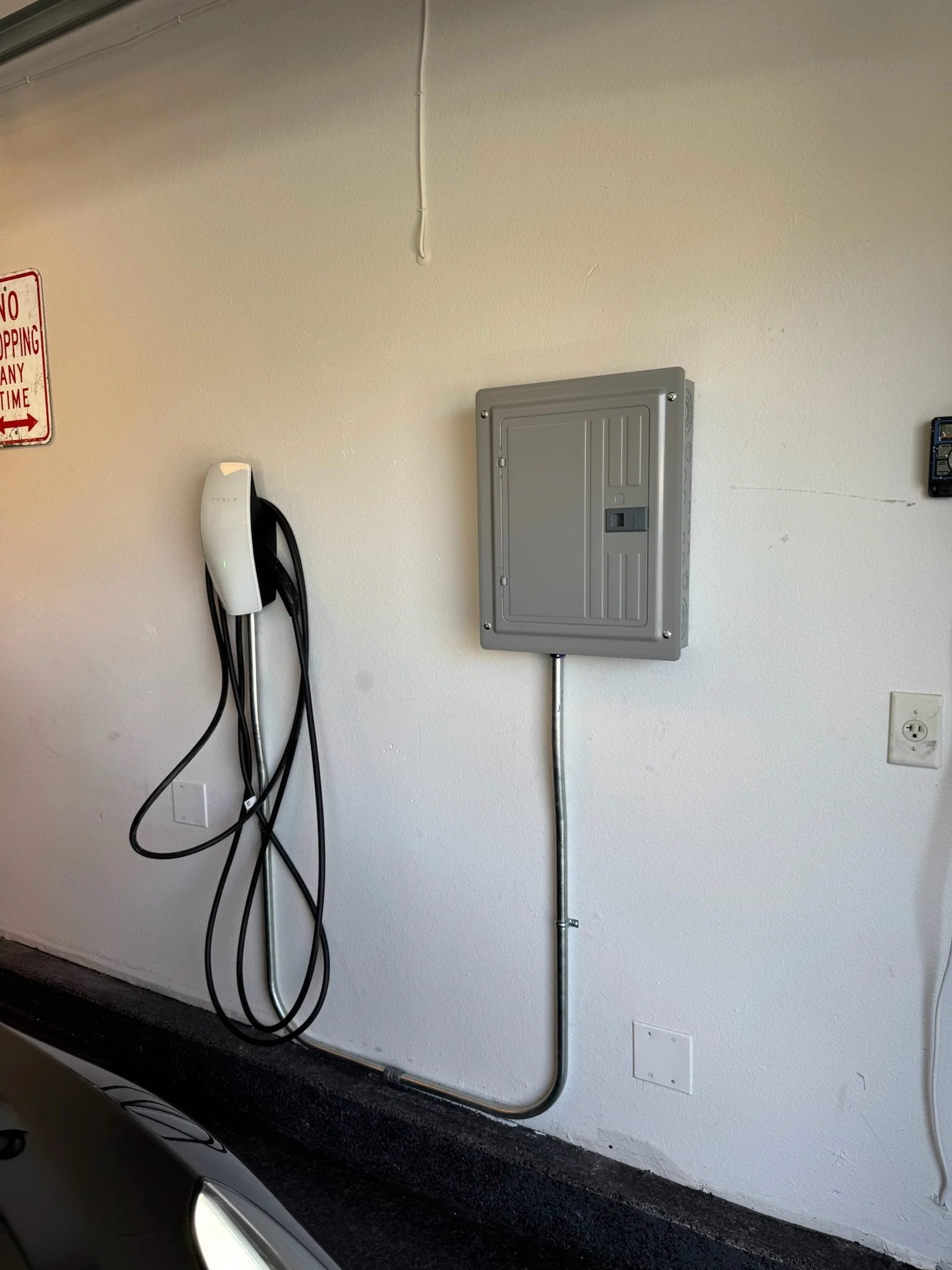 Tesla electric vehicle charging station with a charging cable hanging on the wall.