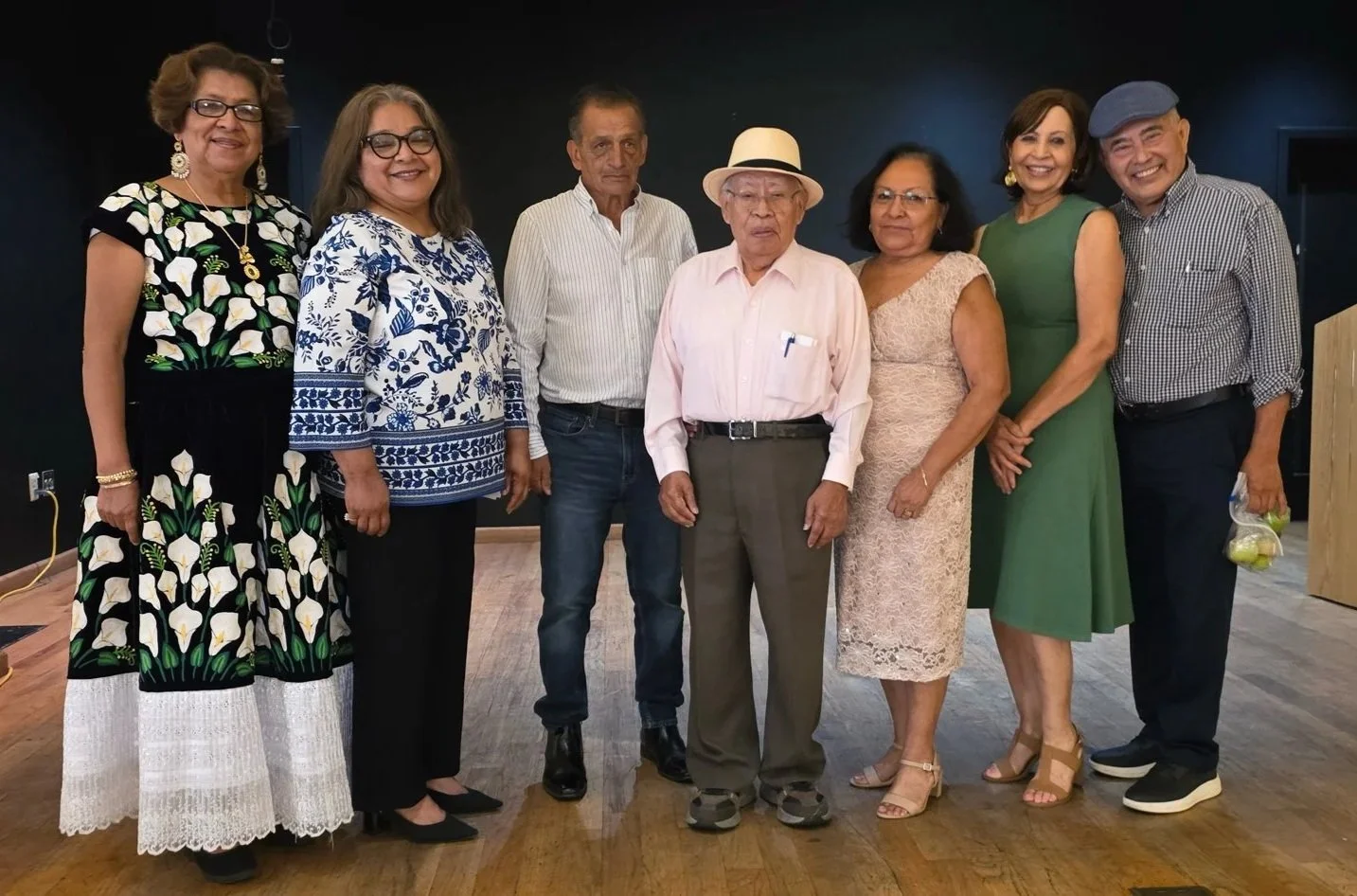 A group of eight adults standing together in a room, posing for a photo, dressed in semi-formal to casual attire.