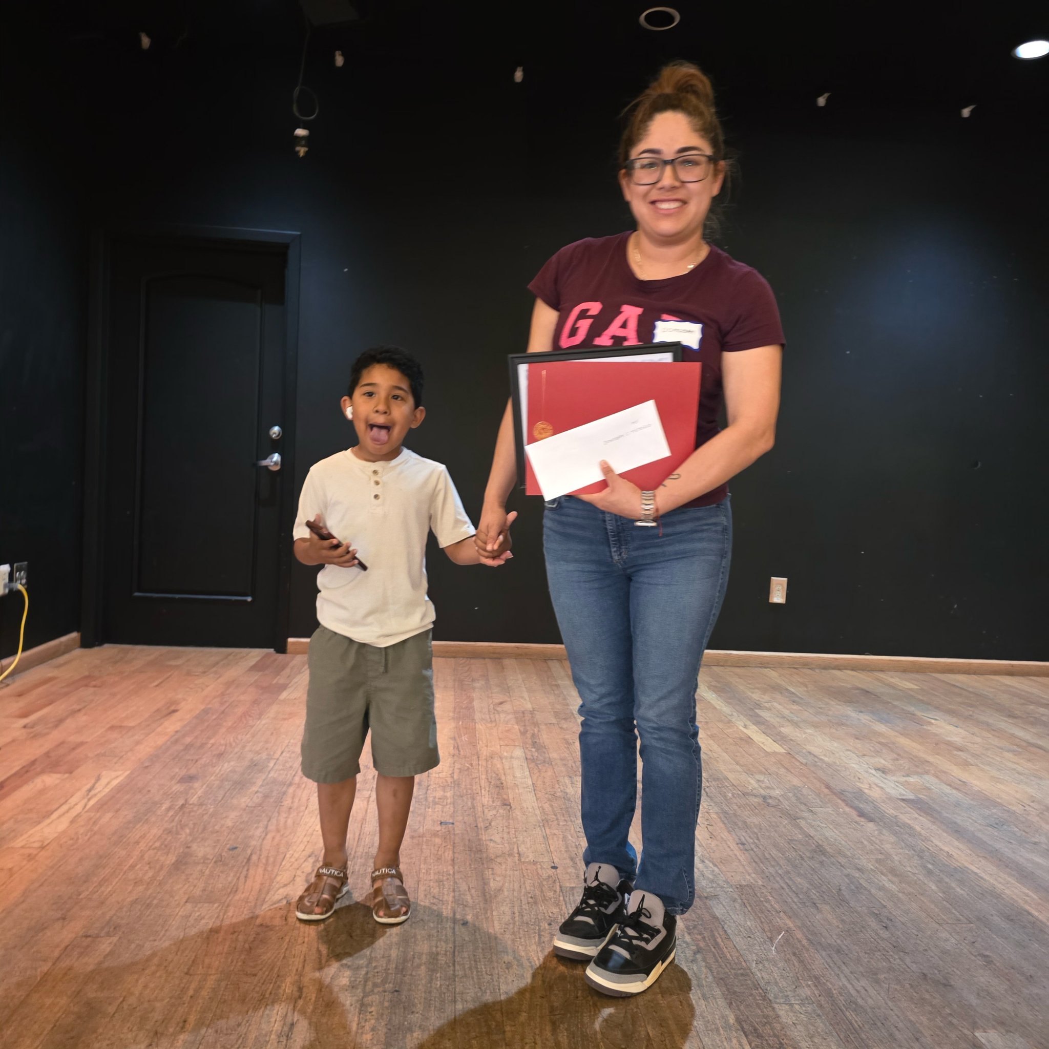 A woman smiling and holding a certificate of scholarship award with a young boy standing beside her.