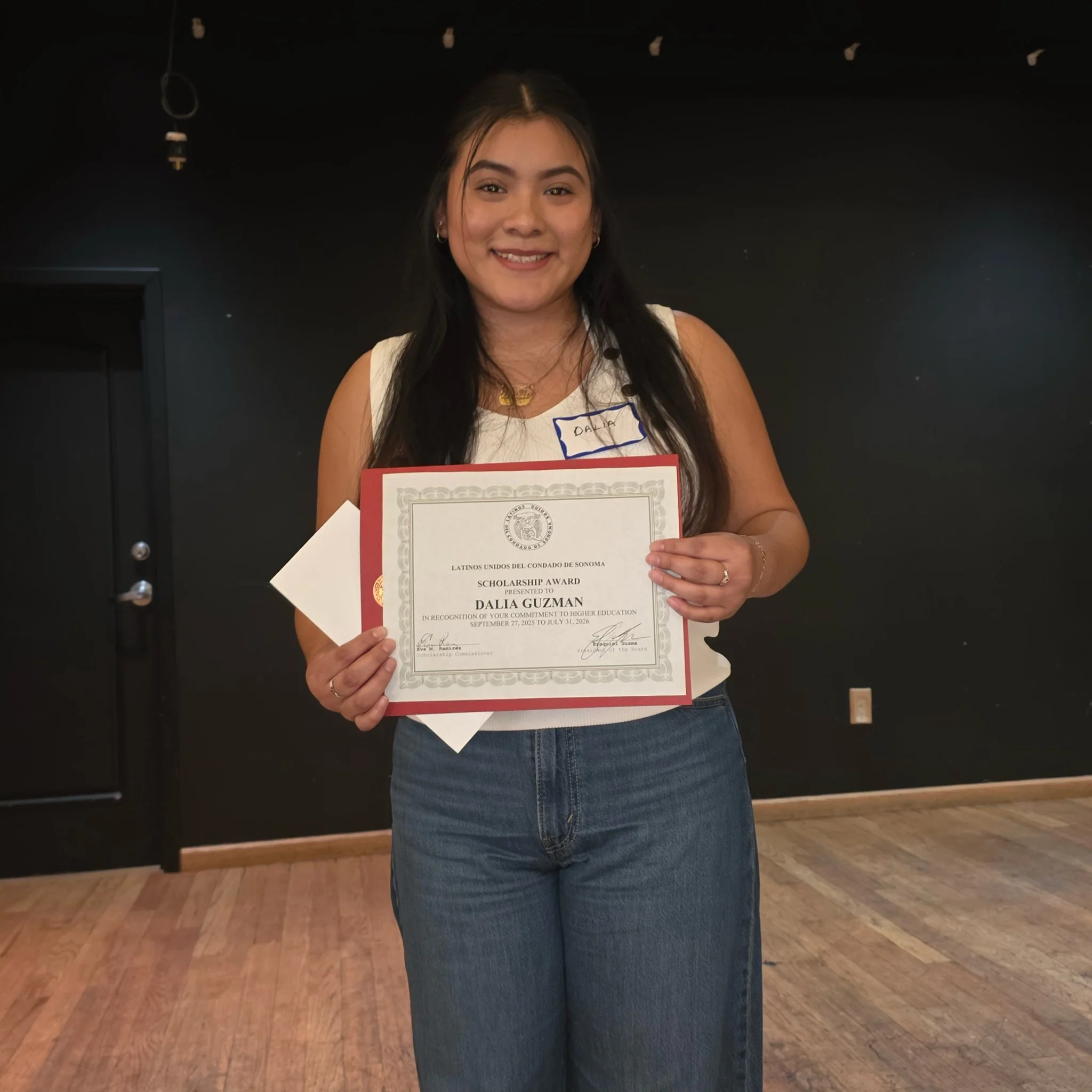 A young woman with long dark hair holding a certificate of scholarship award.