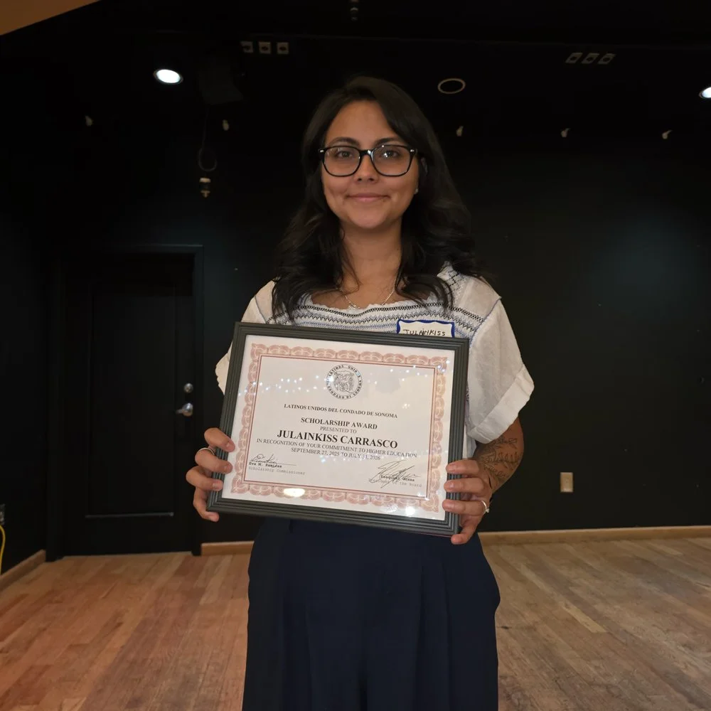A woman with dark hair, glasses, and a white shirt holding a framed scholarship award certificate.