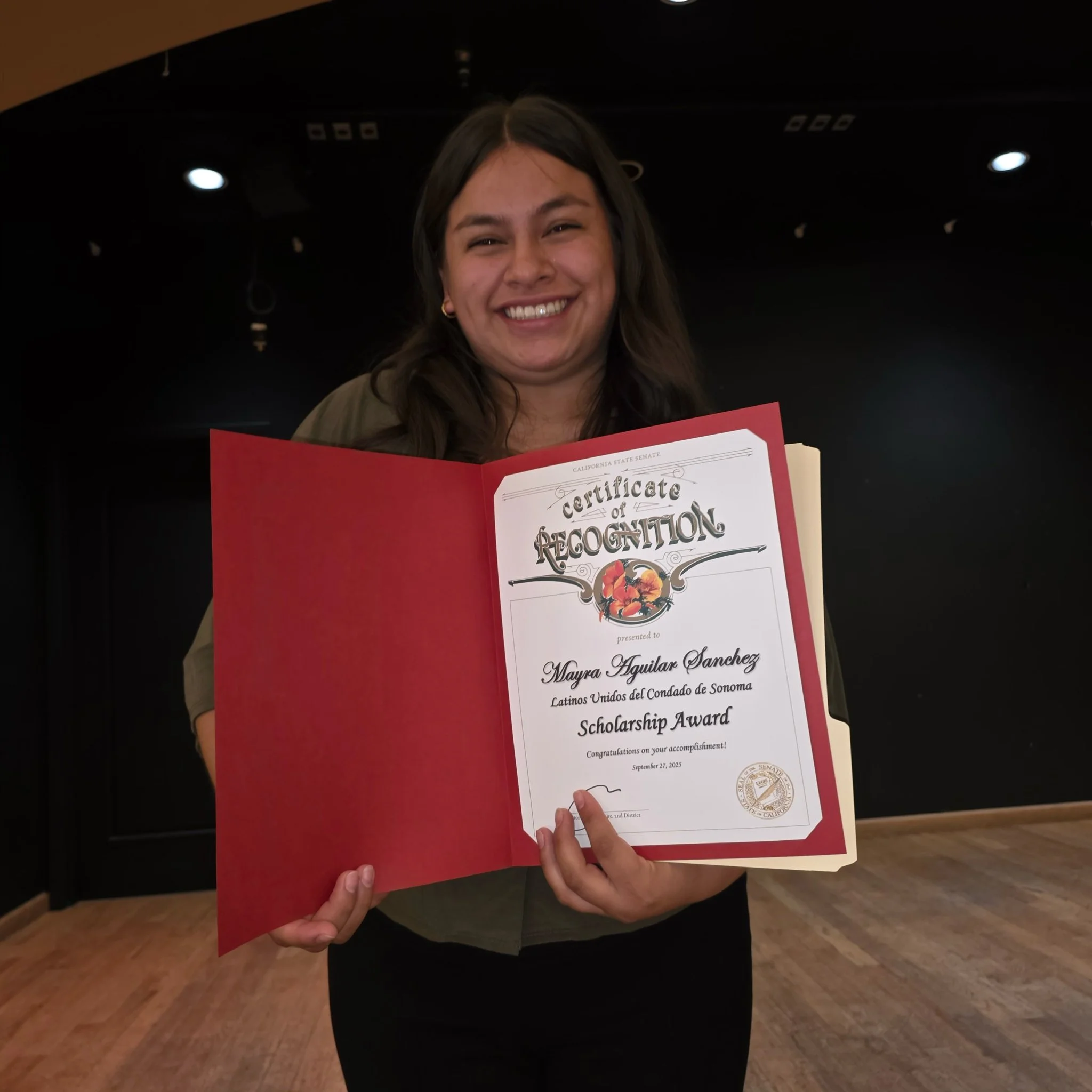 Person holding a certificate titled 'Certificate of Recognition' at an event, smiling for the camera