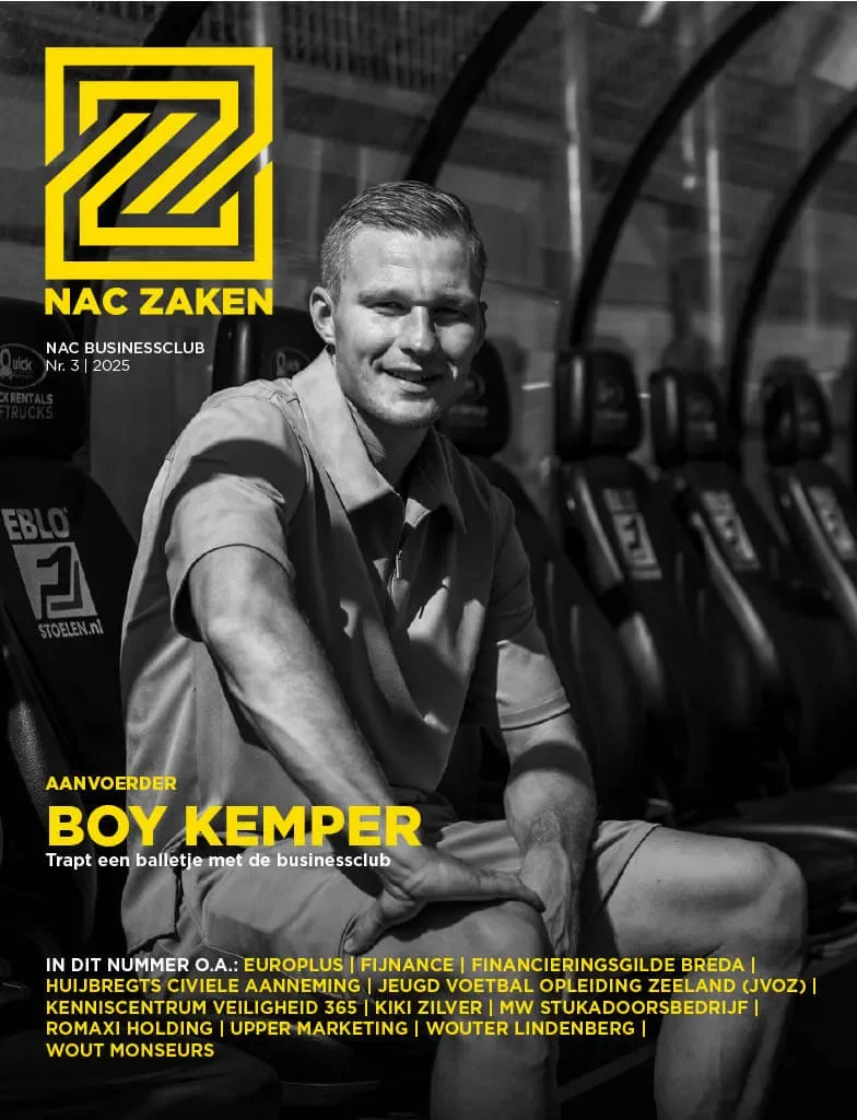 Een zwart-witfoto van een man die op een bank zit in een sportstadion of -hal, met een rij stoelen en een boogvormige structuur op de achtergrond.