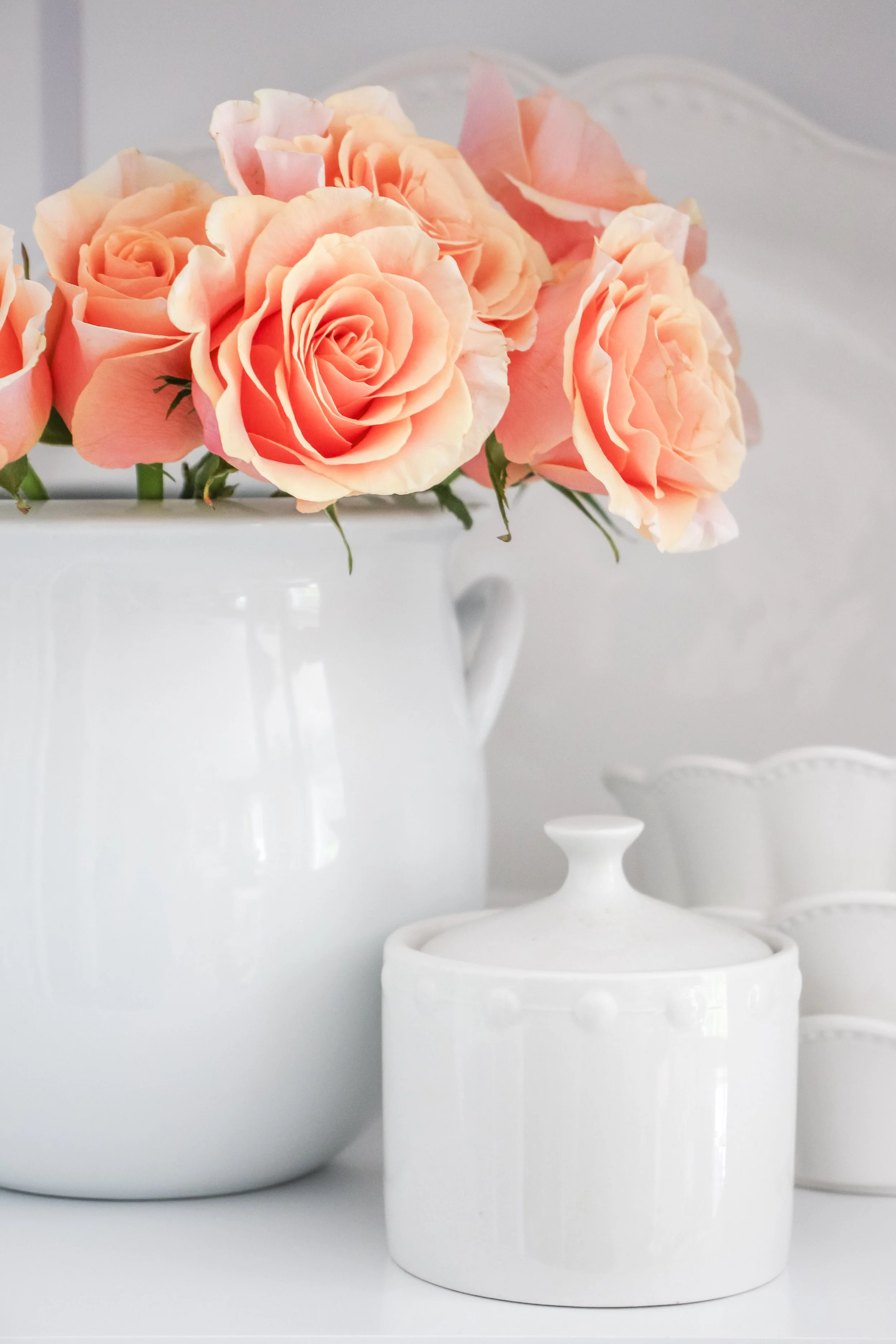 Peach-colored roses in a white vase with matching ceramic containers.