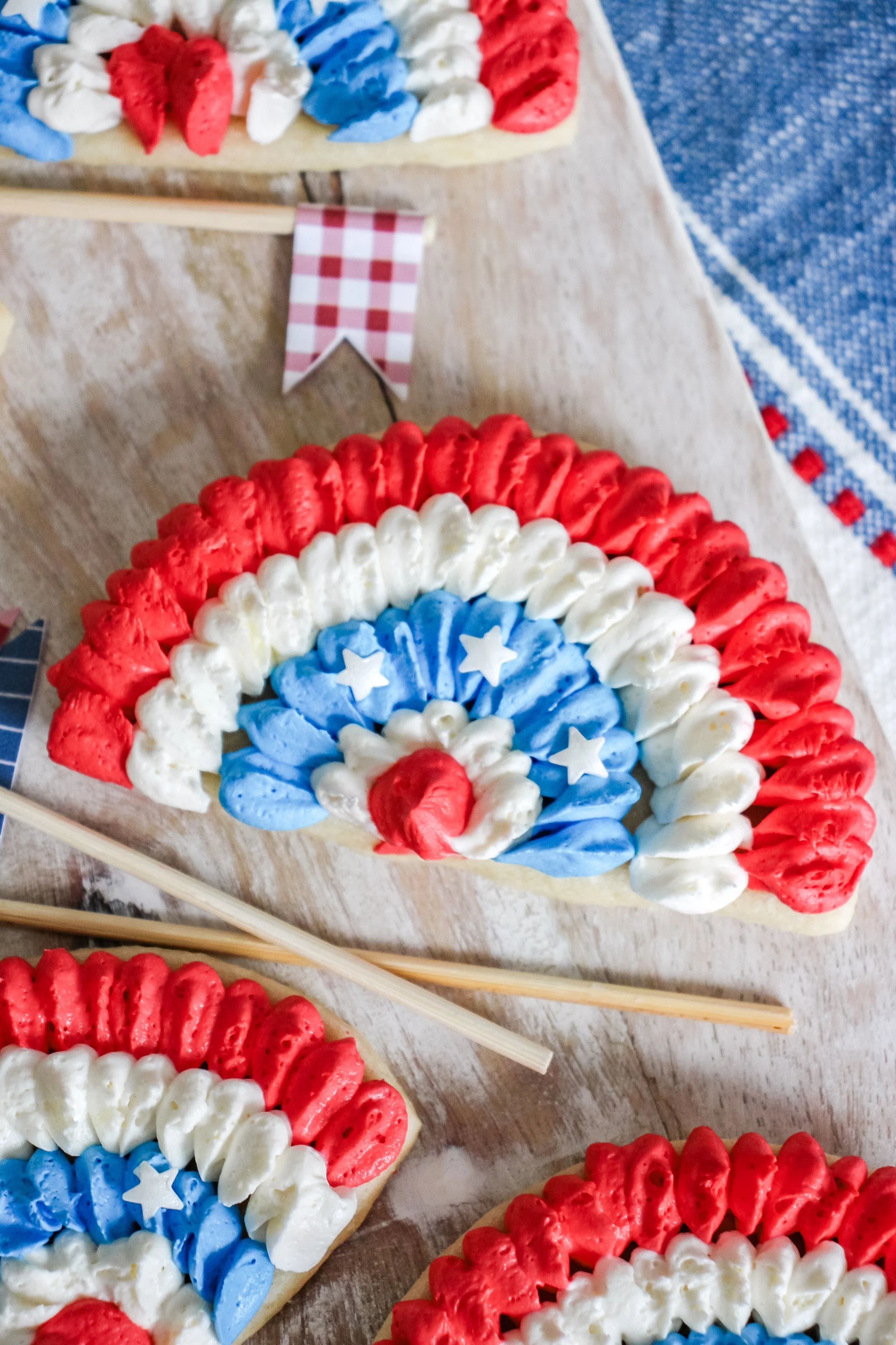 Decorative, patriotic Cookie decorated with red, white, and blue frosting, shaped like a rainbow with stars in the centers, on a wooden surface.