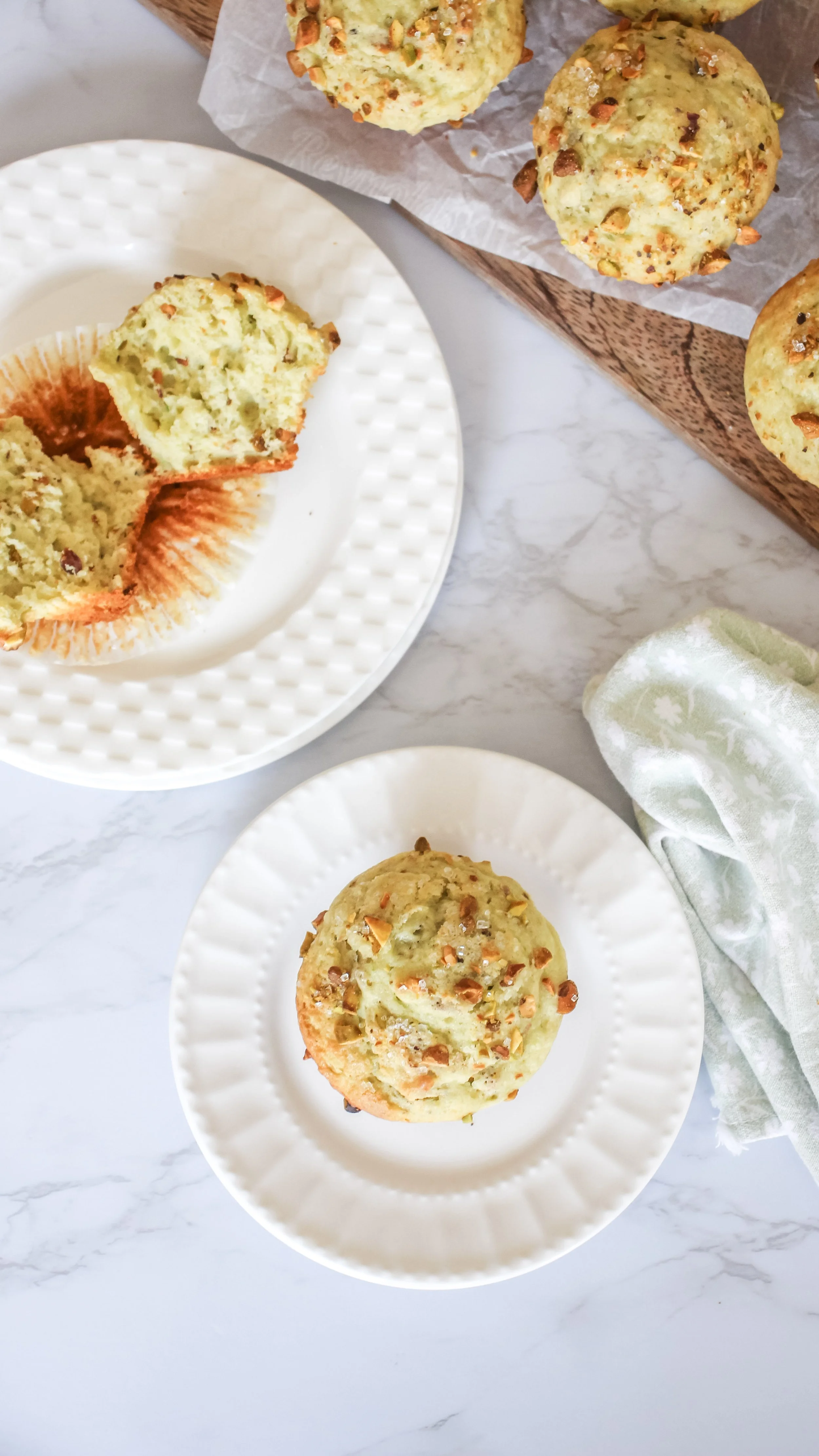 Homemade savory muffins with chopped nuts and herbs on two white plates and a wooden tray, with a green patterned napkin on a marble countertop.