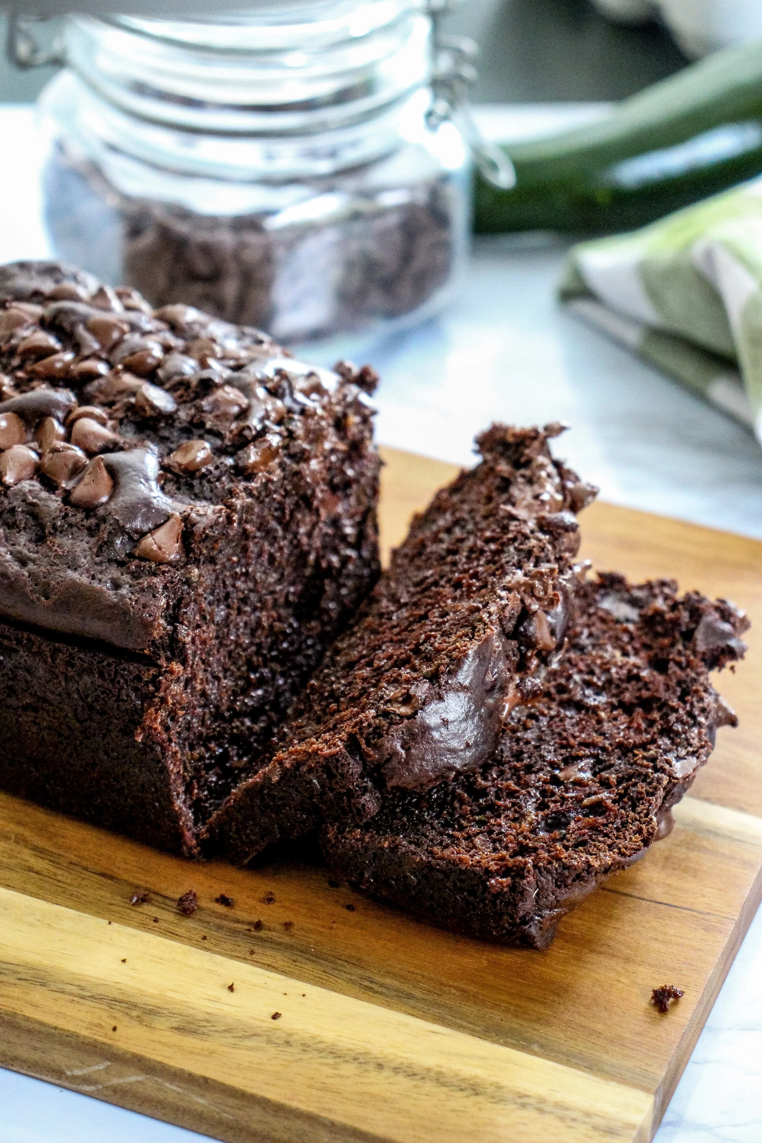 A sliced chocolate loaf cake with chocolate chips on top on a wooden cutting board.