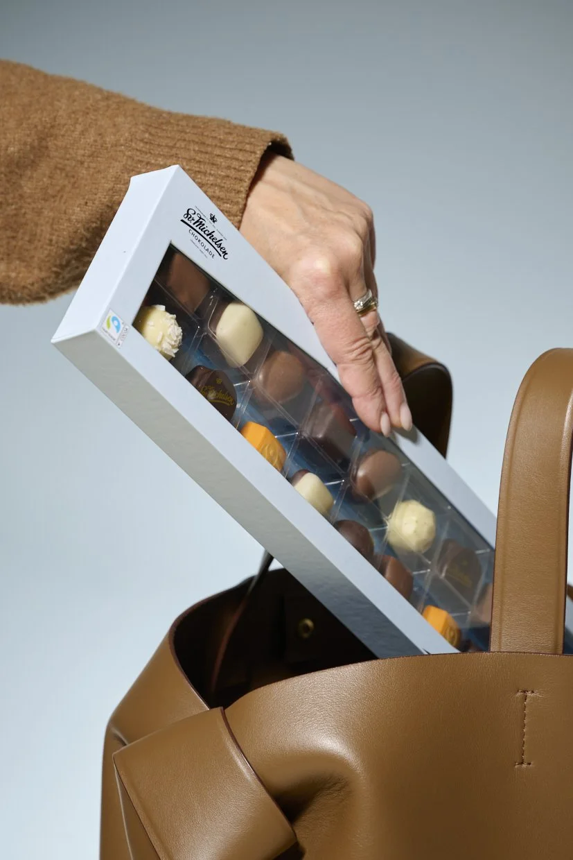 En person tager en æske chokolade ud af en brun lædertaske.