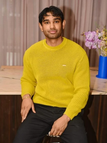 Mand sidder på en stol med en gul sweater foran et bord med en blå vase og blomster.