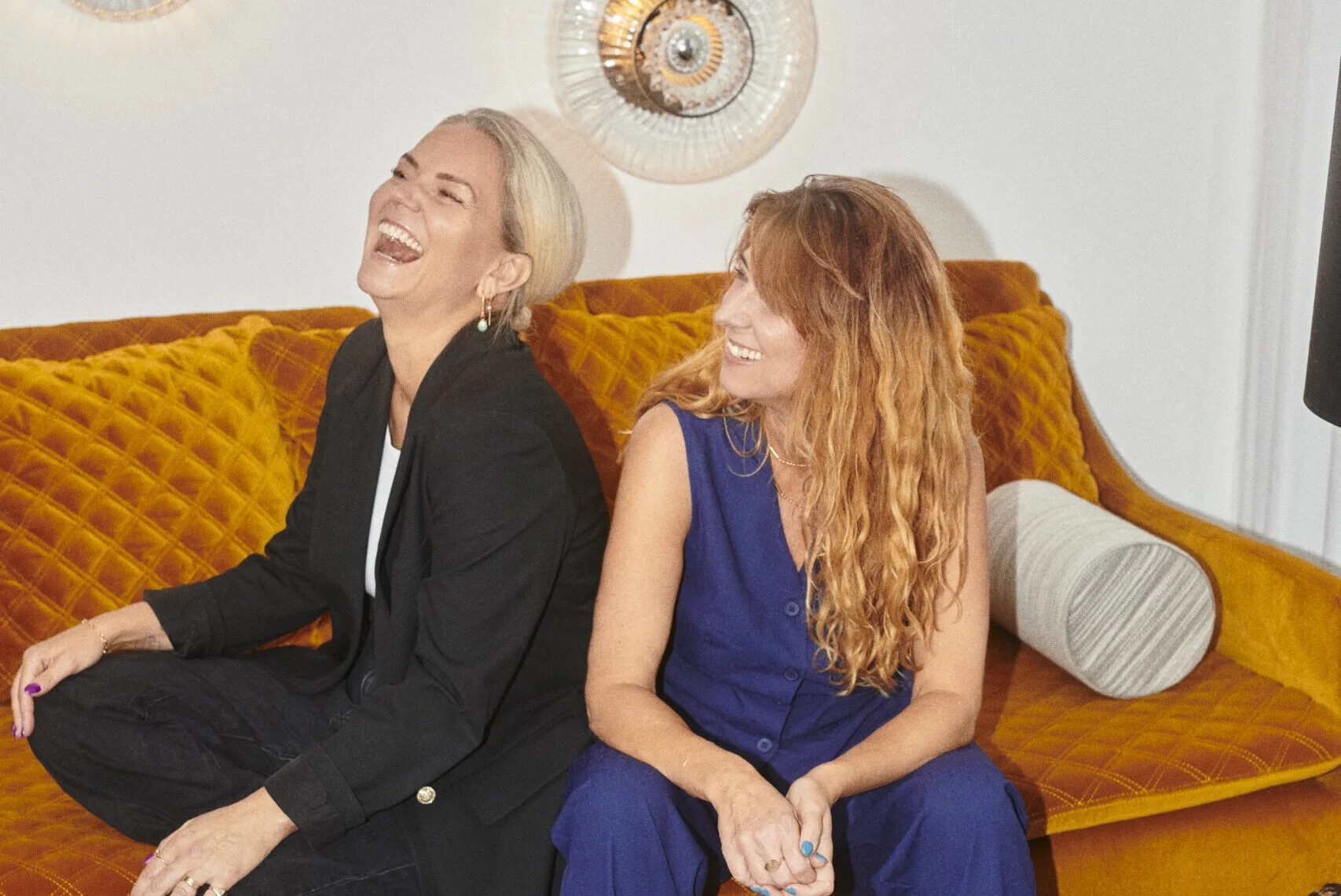 To kvinder sidder på en orange sofa og ler sammen.