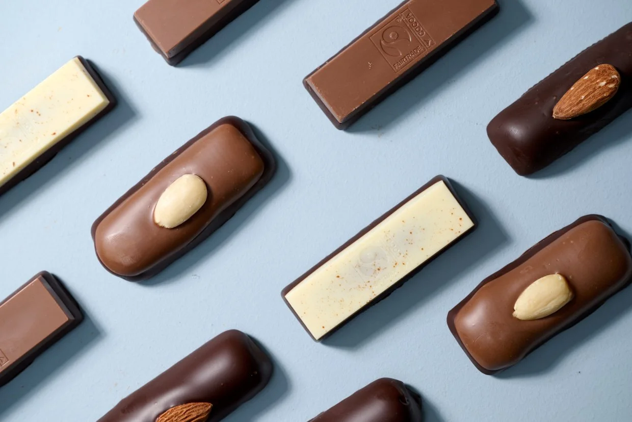 Udvalg af chokoladebarer med forskellige former og toppings på en lyseblå baggrund.