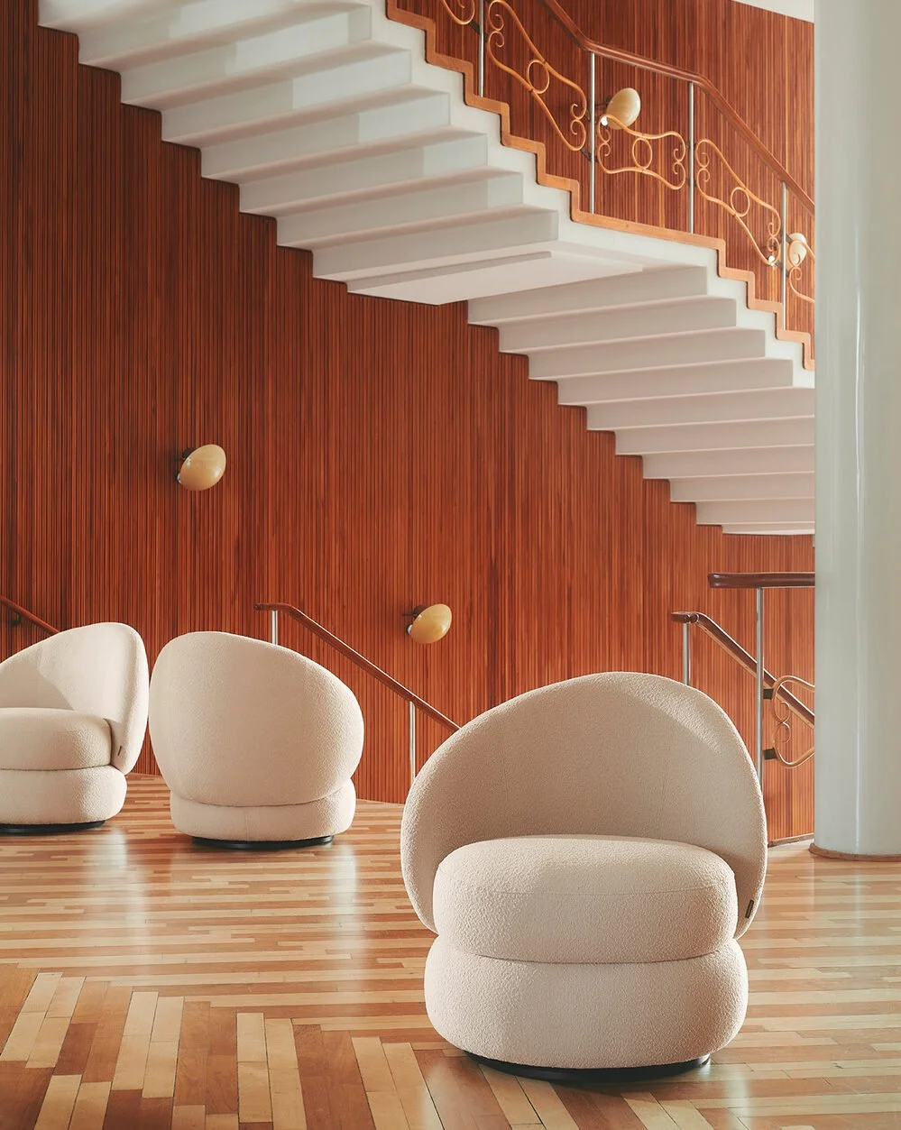 Moderne indretning med lyse, bløde stole, trappe med guldgelændere, træt væg og trægulv.