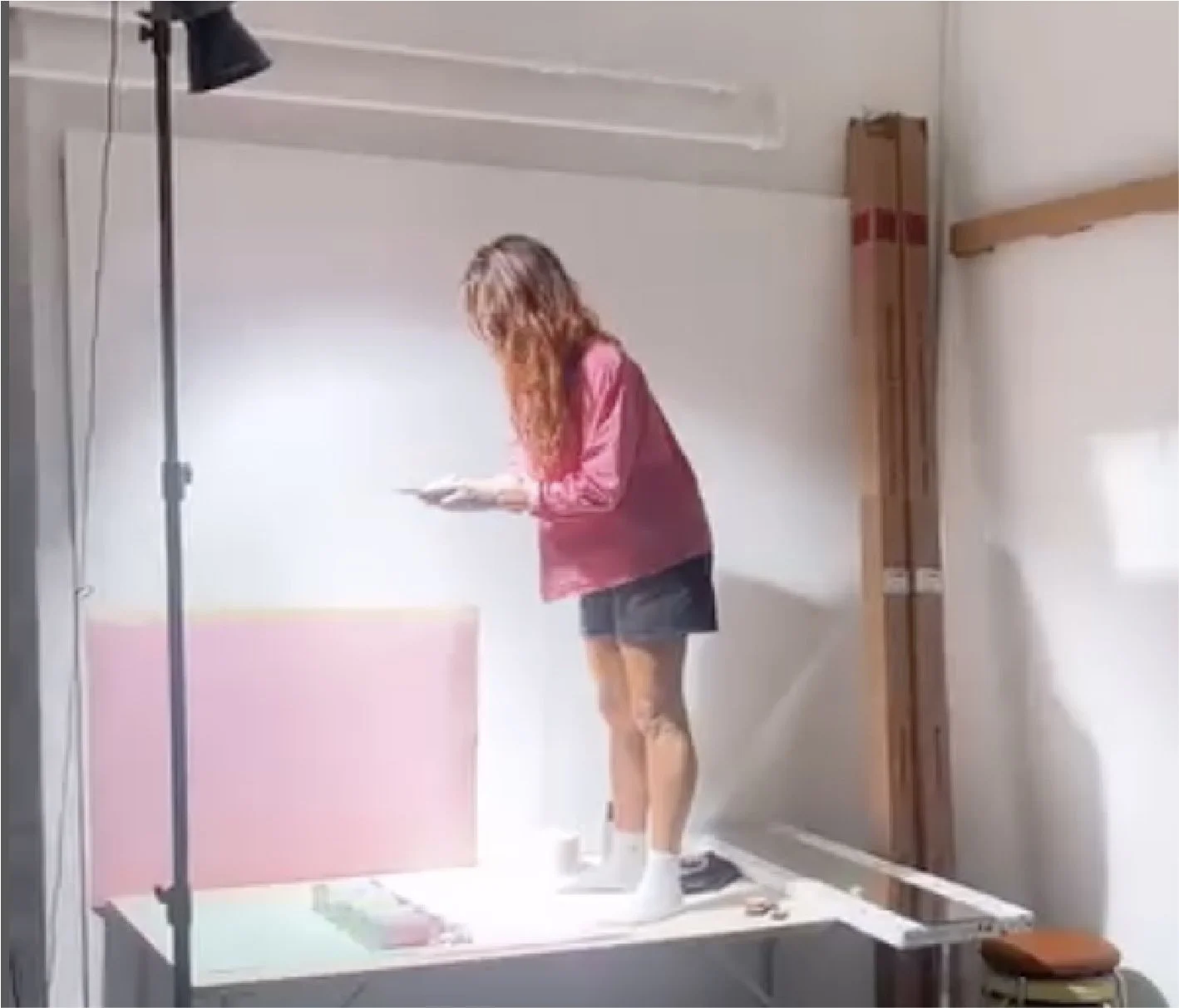 Kvinde står på en platform, som er indrettet som en fotostudio, med lysudstyr, og bruger en mobiltelefon.