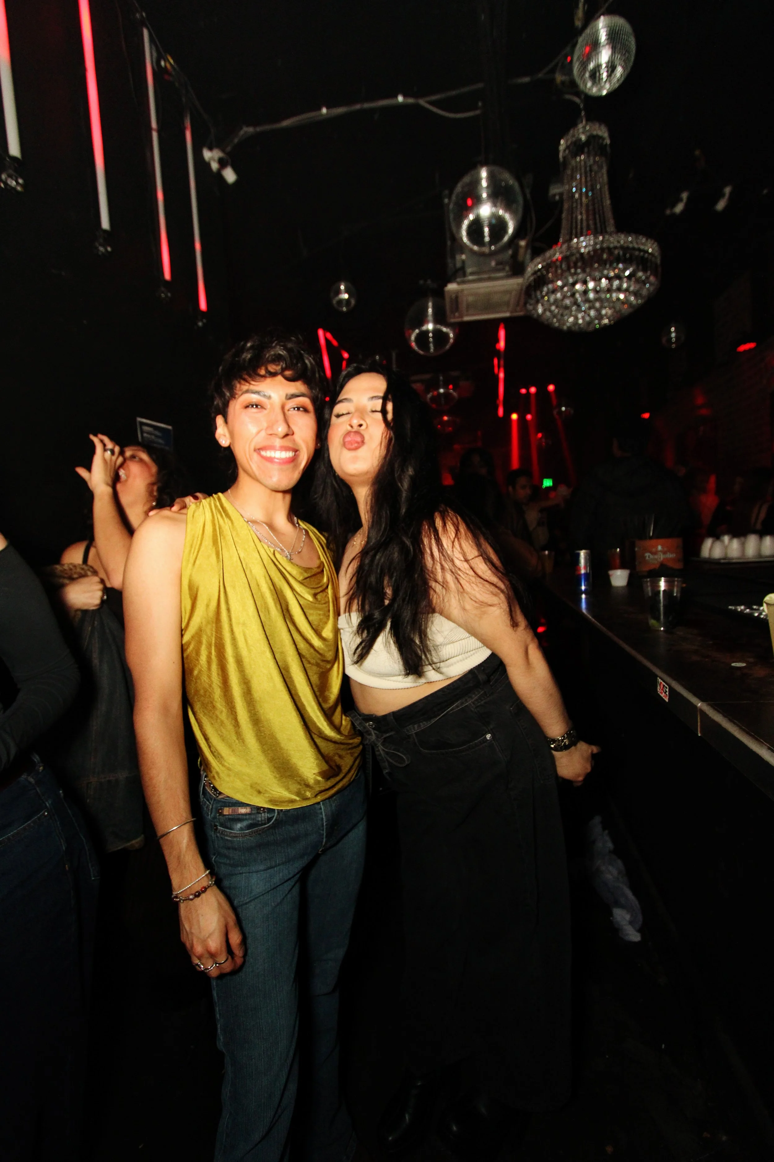 Two women celebrating in a nightclub with disco balls and red lighting in the background.