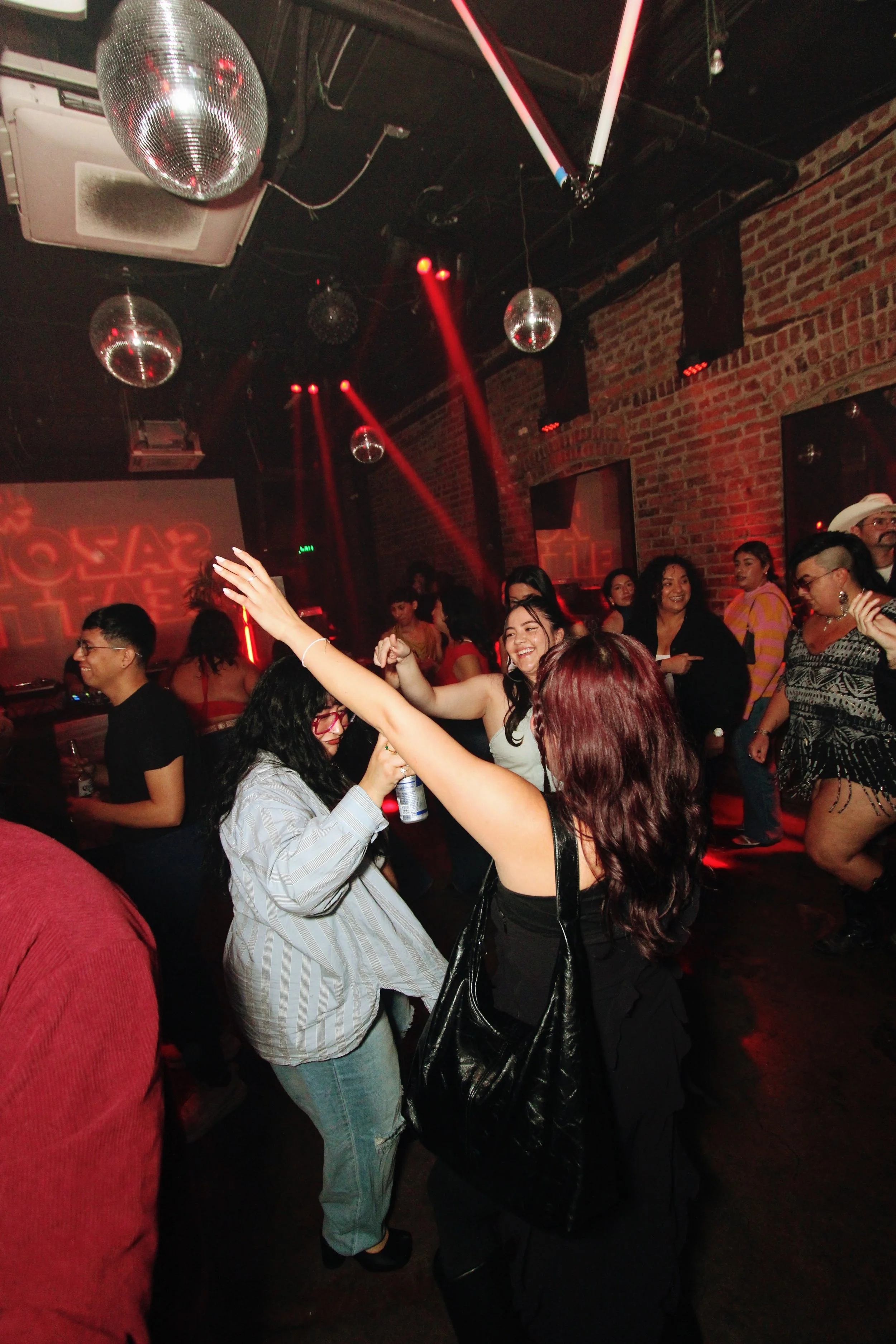 People dancing and having fun in a nightclub with red lighting, disco balls, and brick walls.