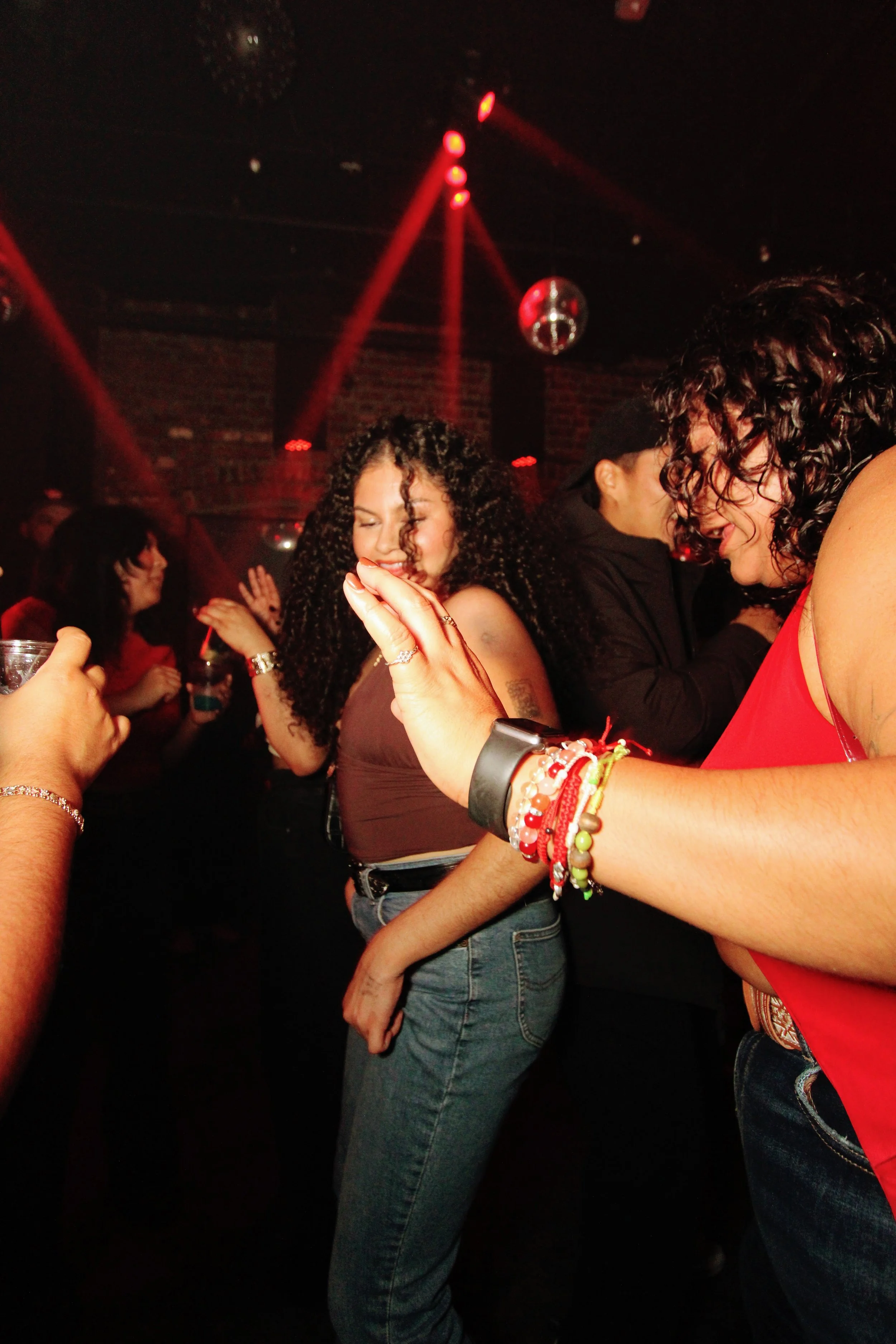 People dancing and having fun in a nightclub with red lighting and disco ball.
