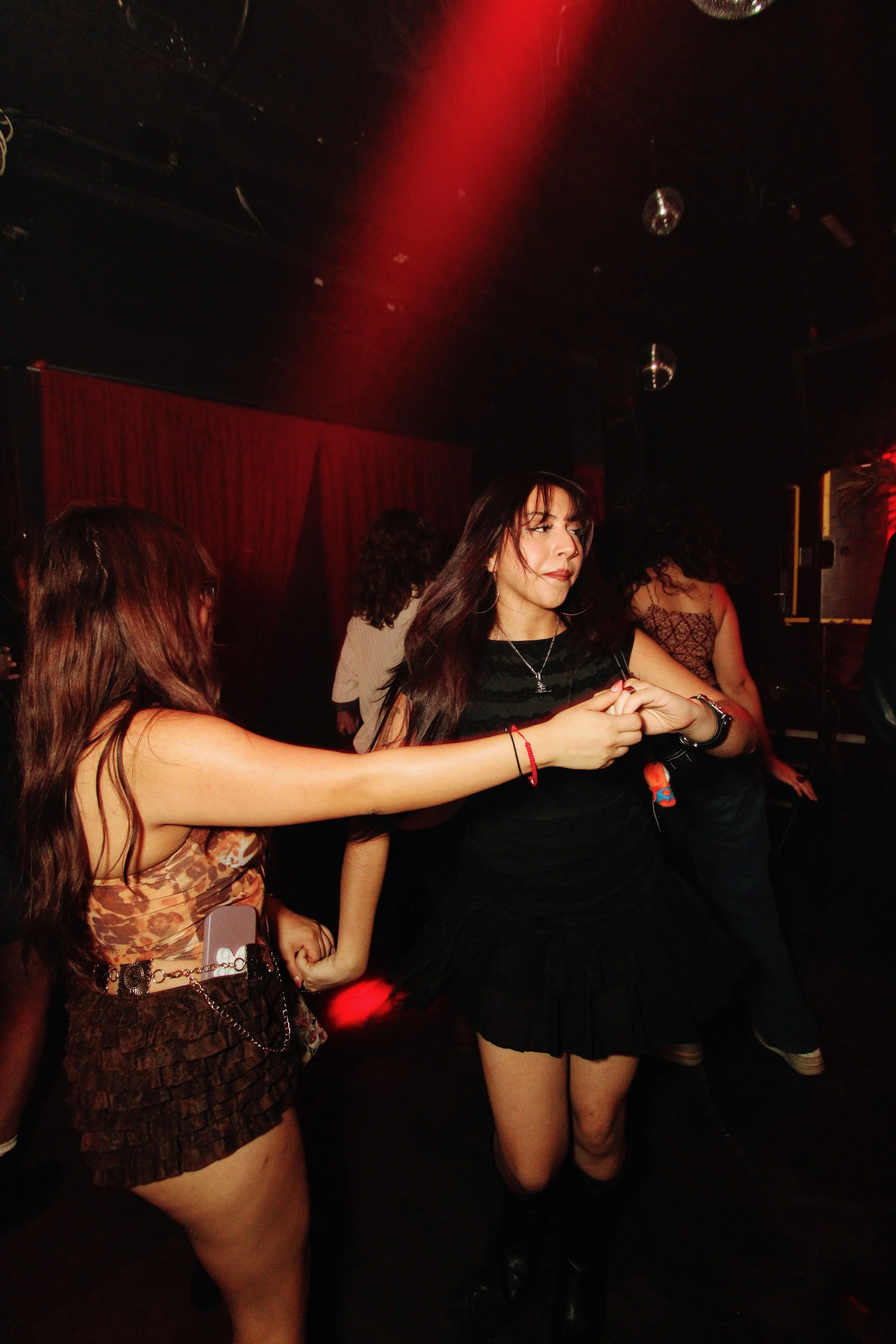 Women dancing and enjoying themselves in a nightclub with red lighting and disco balls.