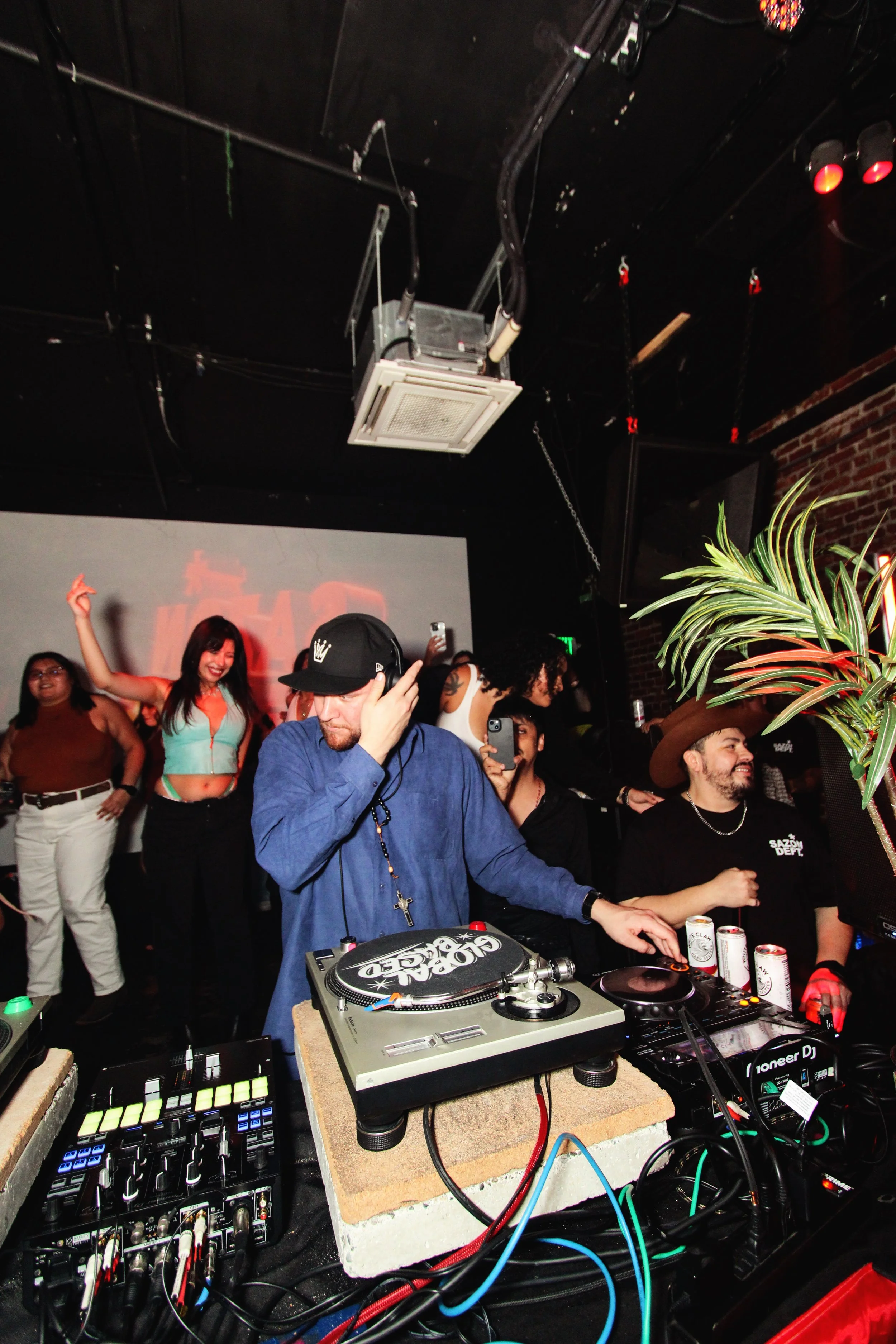 DJ performing at a party with people dancing and enjoying in the background.