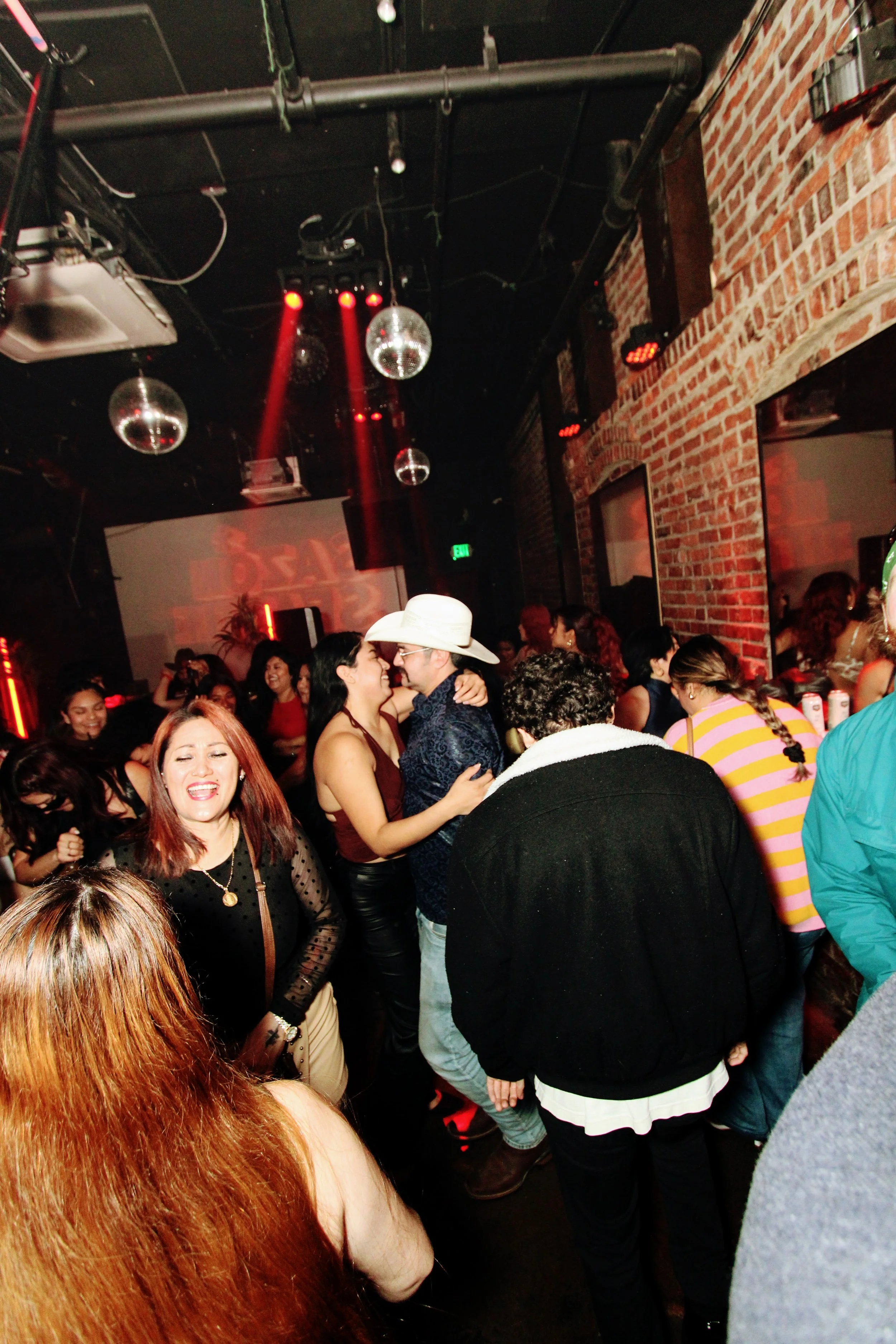 People dancing and socializing at a nightclub with brick walls and disco balls overhead.