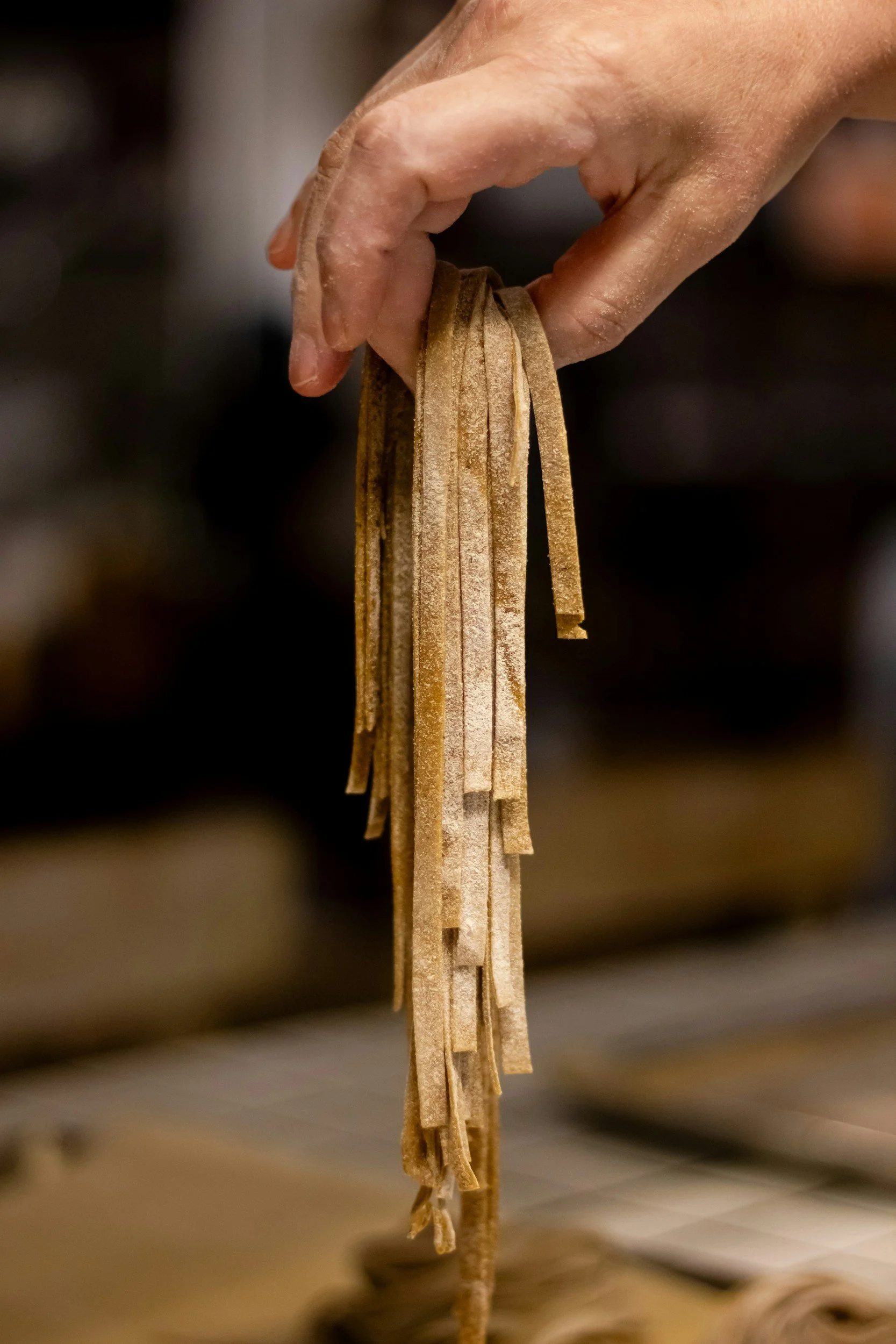 A person's hand holding a bundle of uncooked, dried pasta strands.
