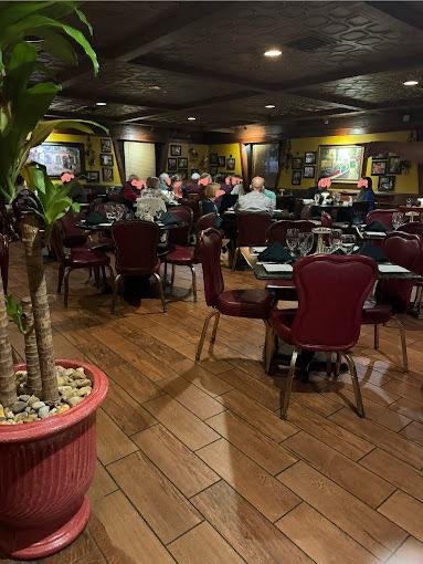 Interior of a restaurant with dining tables and chairs, some diners seated, warm lighting, wooden flooring, and framed pictures on the yellow walls.