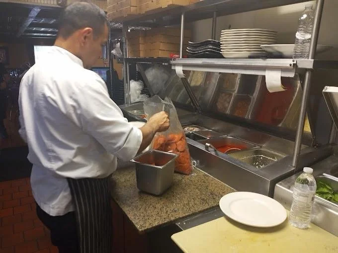 Chef preparing food at a kitchen counter with plates, water bottle, and food containers.