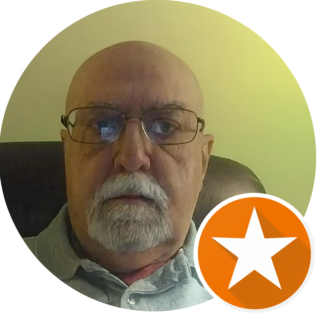 Close-up of an older man with glasses, a white beard, and a serious expression, sitting in a chair with a light-colored wall behind him, featuring a star icon on the lower right.