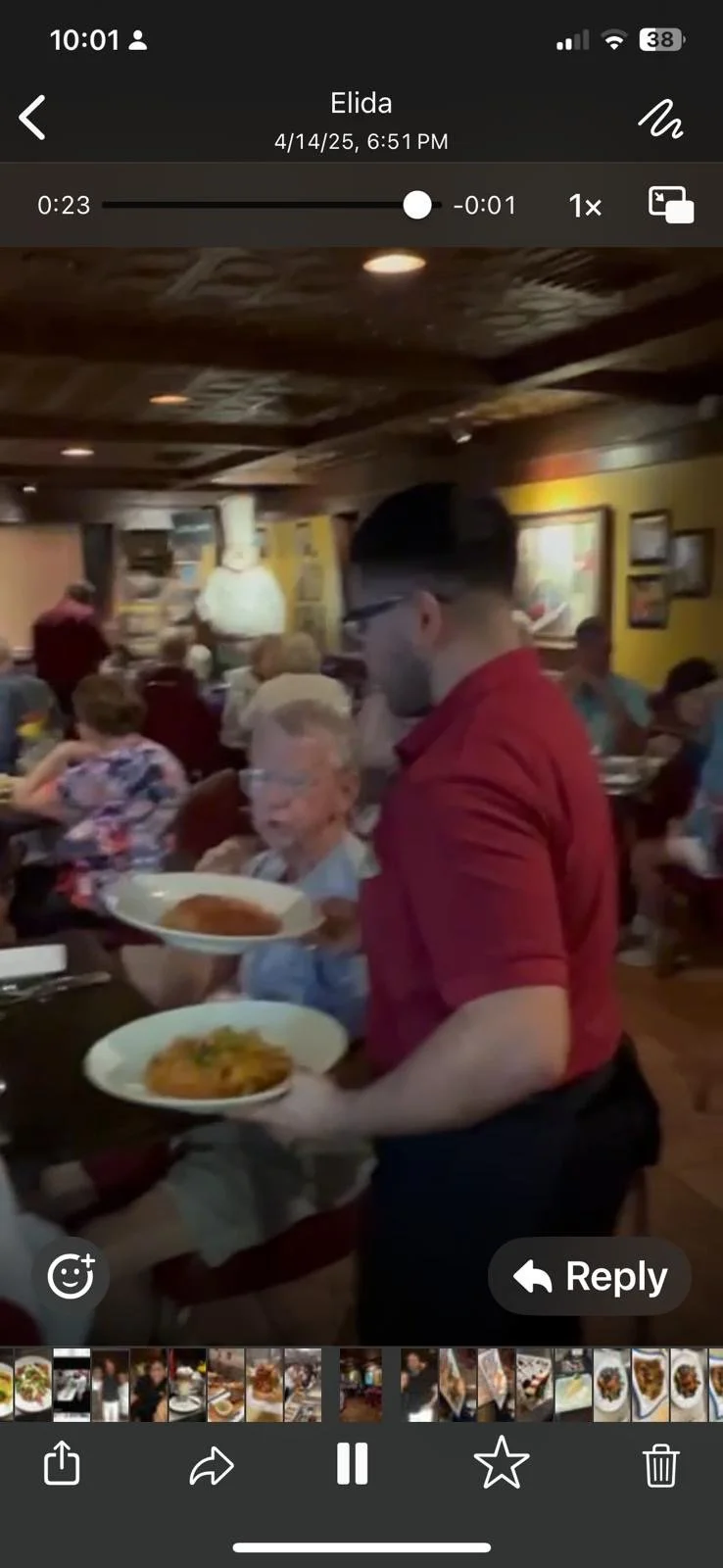 A waiter in a red shirt and glasses serving plates of food in a crowded restaurant with several patrons dining and colorful wall decorations.