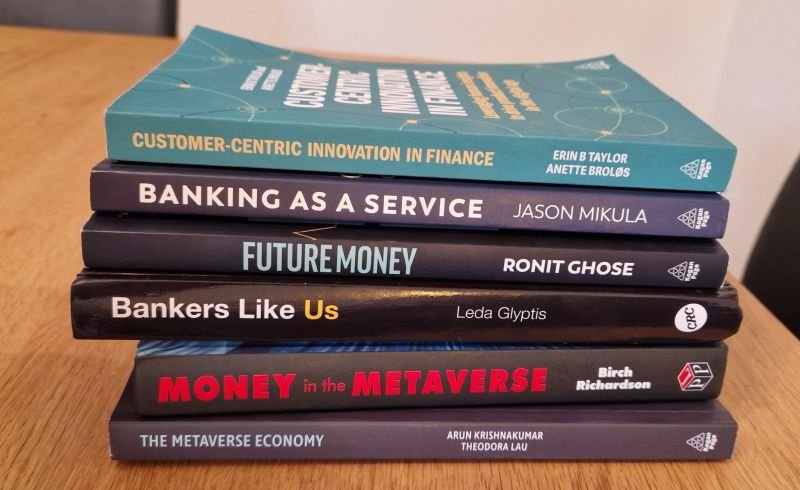 Stack of seven finance and banking books on a wooden surface.