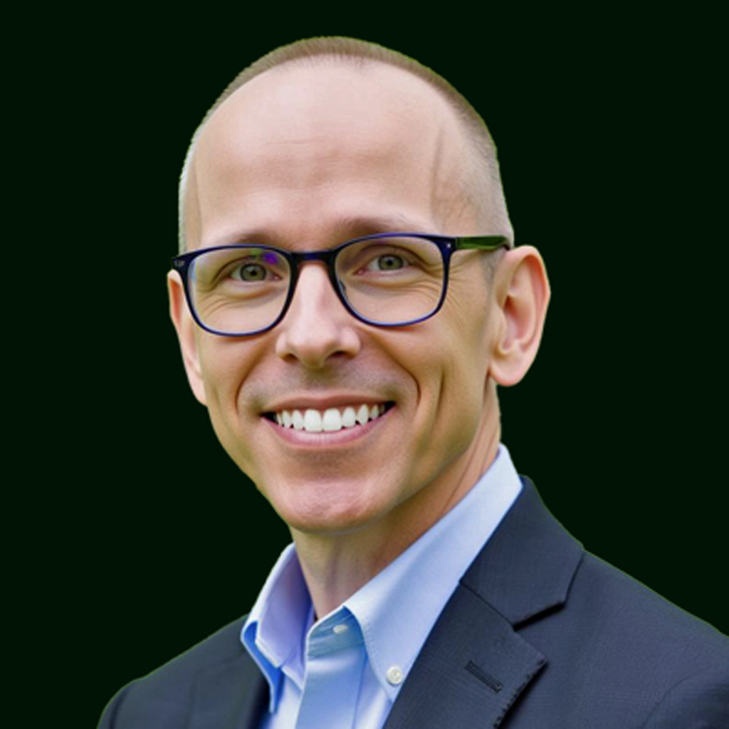 Headshot of a smiling man with glasses, wearing a suit and light blue shirt, against a dark background.