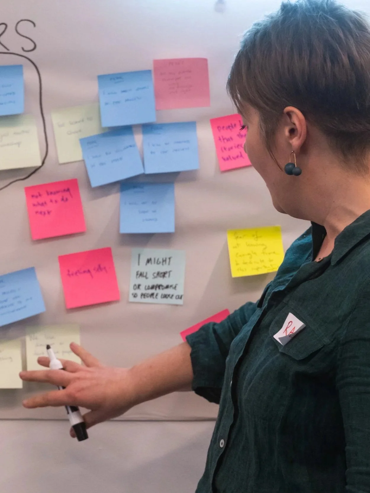 A person holding a texta and standing in front of a wall with post-it notes.