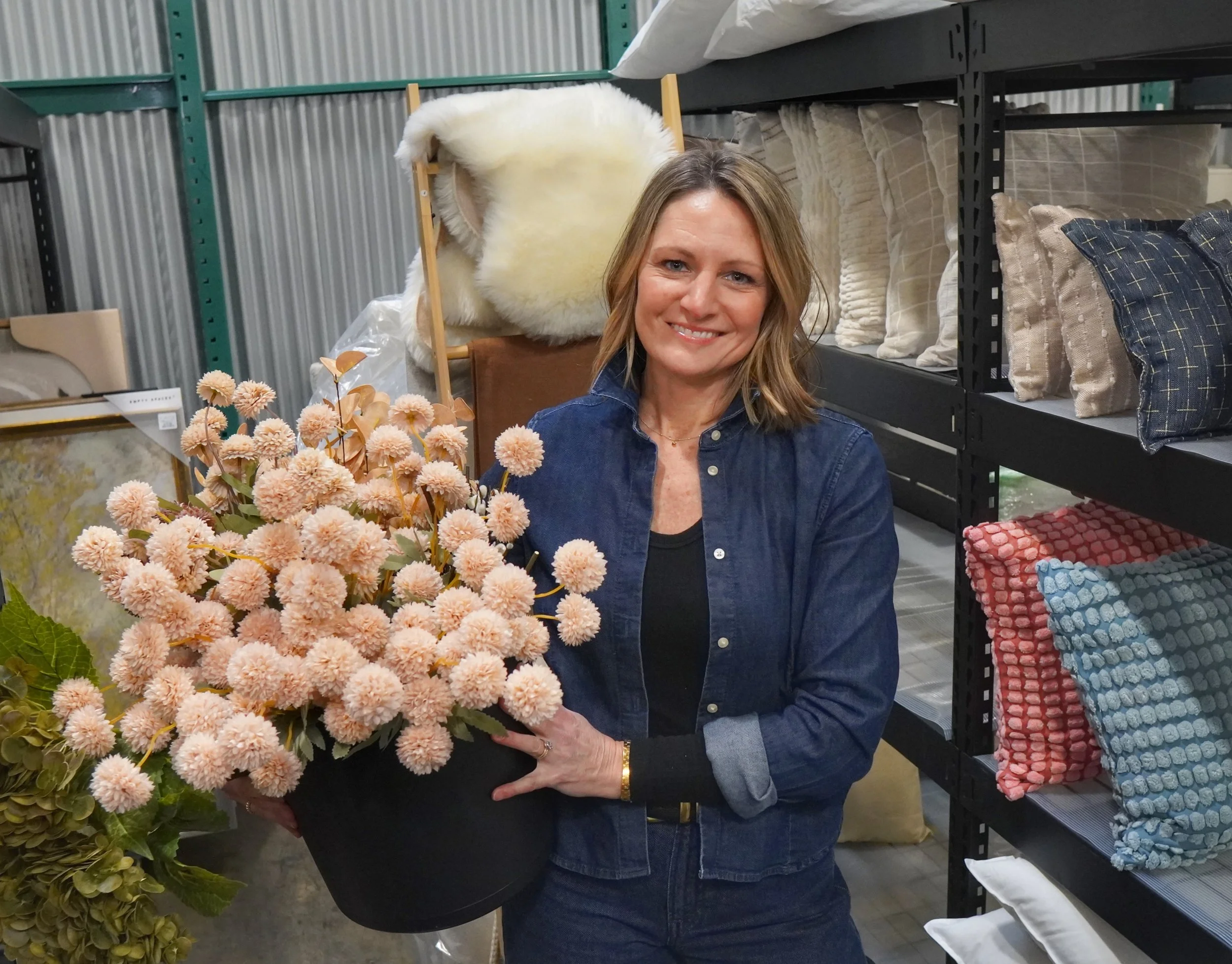 Becky in the warehouse holding a pot of faux flowers.